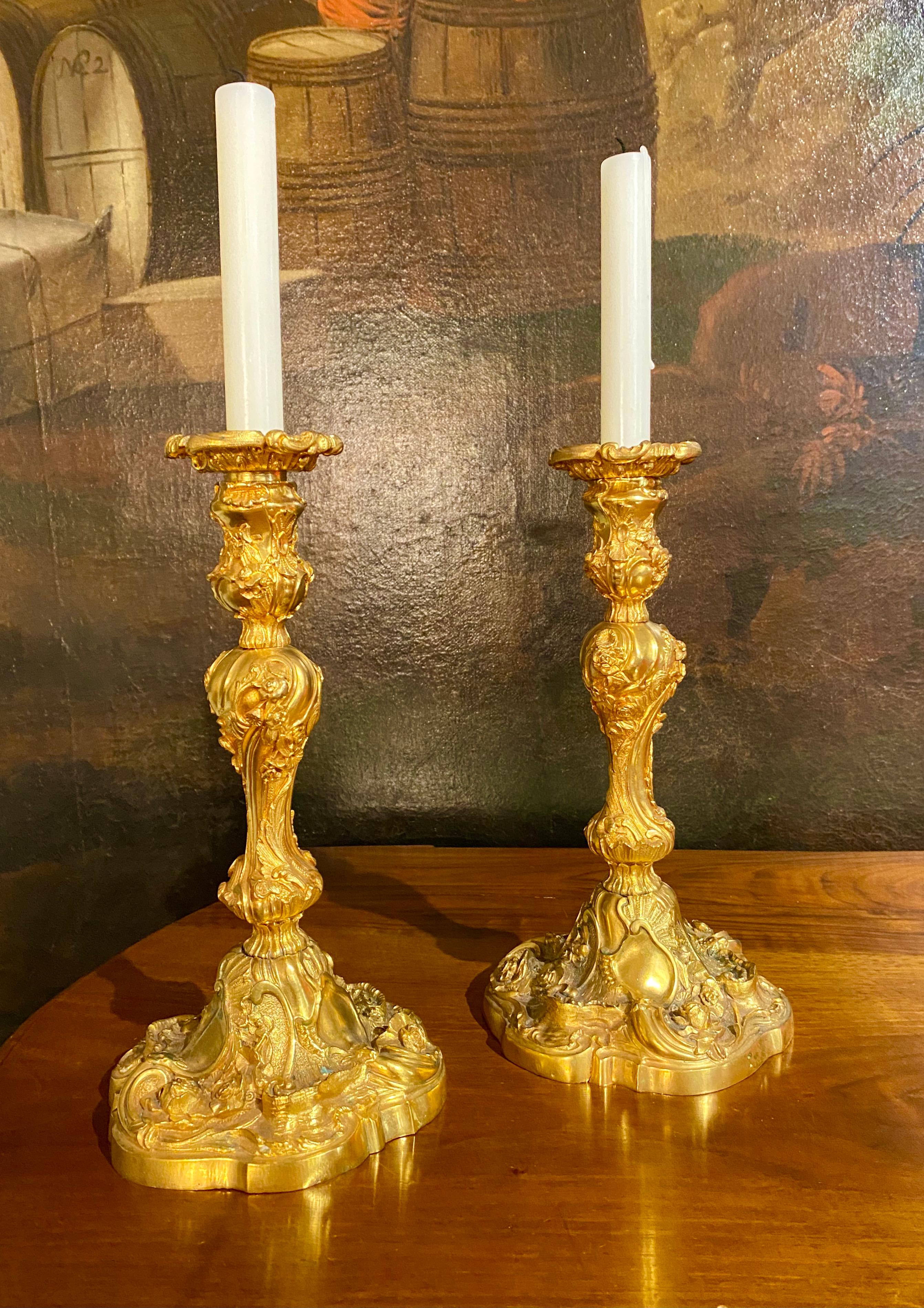 Paire de chandeliers en bronze doré finement ciselé de style Louis XV. Les bases complexes sont décorées de fleurs, de guirlandes, de volutes et de coquillages. Rocaille et godrons tournent autour de la tige dans le style baroque et rococo, et