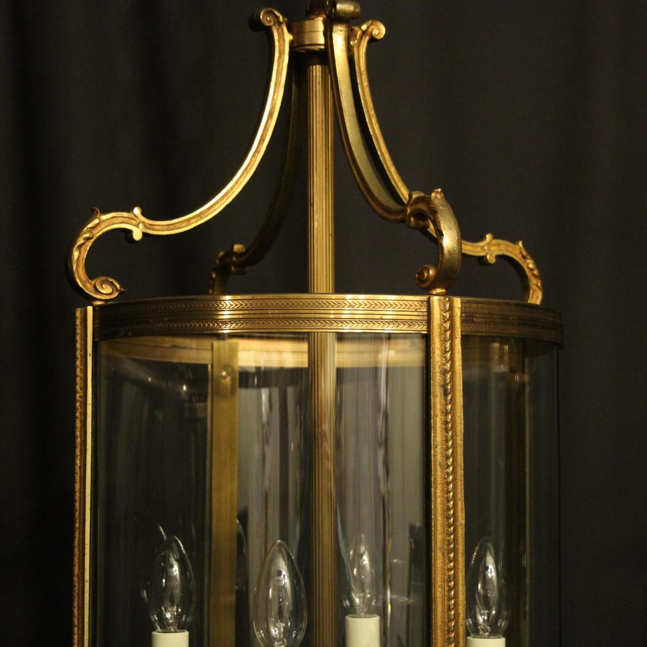 A French pair of large gilded bronze four light convex antique lanterns, the four scrolling light fittings surrounded by four sectional circular convex glass panels and held within a decorative leaf scrolling framework with barley twisted side