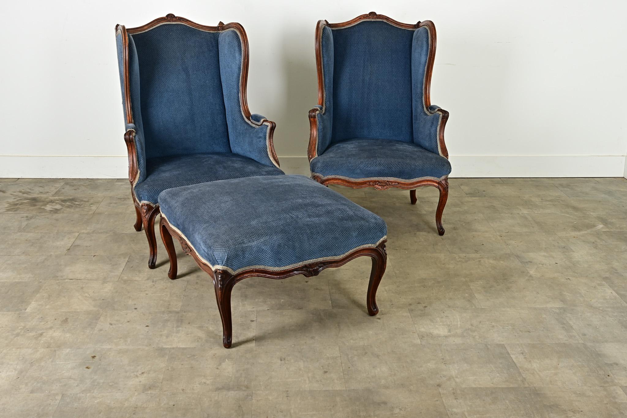 Une paire sophistiquée de fauteuils bergères à dossier ailé du 19ème siècle français et un grand ottoman assorti. L'un des côtés de l'ottoman est concave pour s'adapter à l'avant arqué de la chaise - formant ainsi une sorte de chaise longue - et