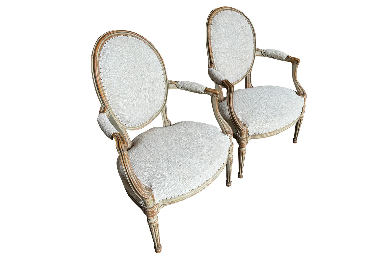 Preciosa pareja de sillones de estilo Luis XVI procedentes del sur de Francia.  Fabricada por expertos en madera de haya, con maravillosos detalles tallados y volutas en los brazos y patas cónicas estriadas.  Un complemento elegante para una sala de