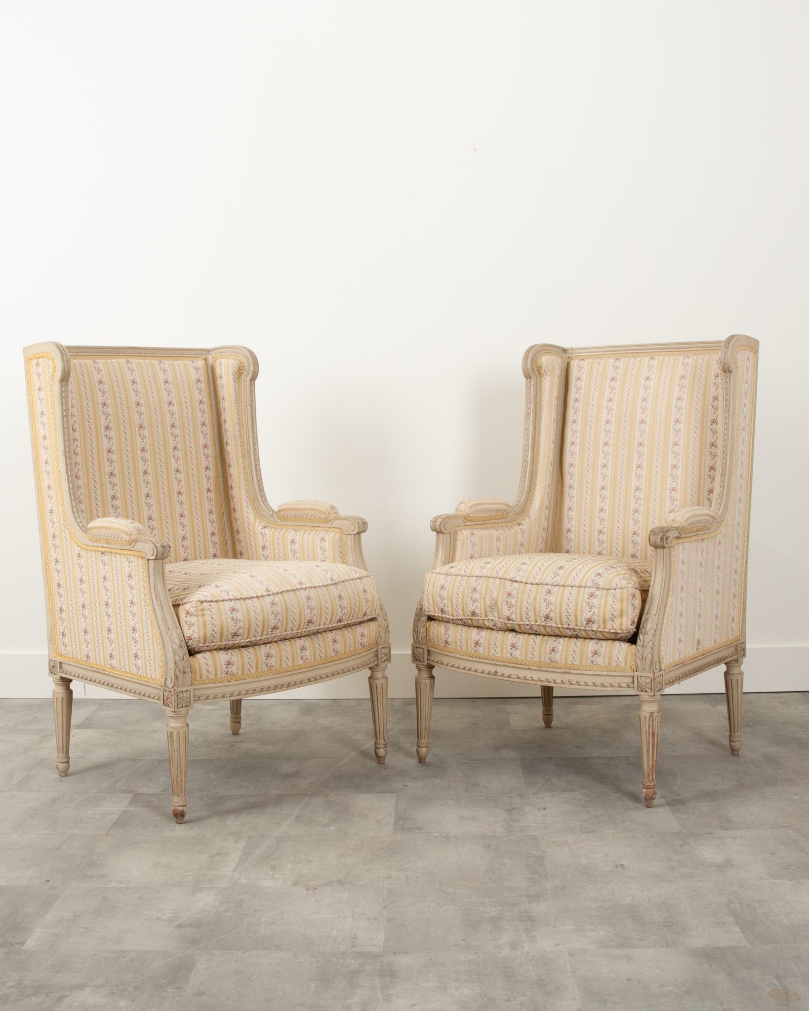 This pair of French Louis XVI-Style bergeres are in wonderful condition. The frames are 19th century, hand carved with a twisted ribbon border, acanthus leaf arms, and painted in its original finish. Upholstered in elegant stripe floral fabric with