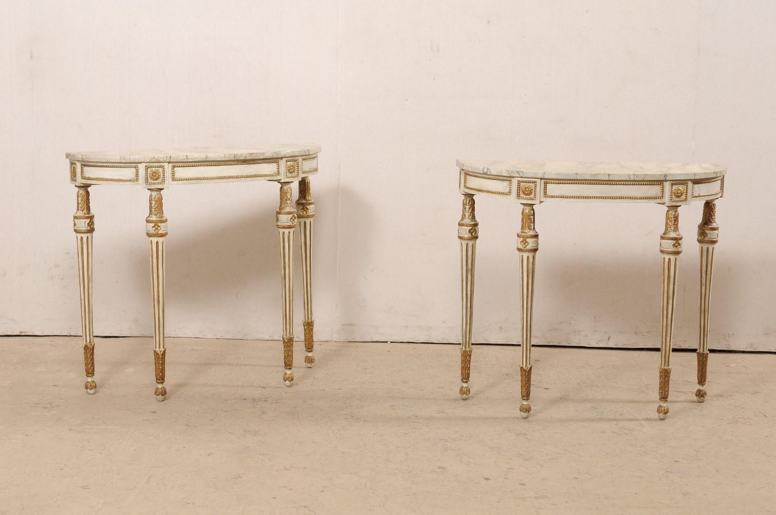 A French pair of Louis XVI style console tables from the early 20th century. This antique pair of console tables from France each feature elongated half-moon faux marble tops, atop a Louis VXI style wood base with rounded apron adorned in petite
