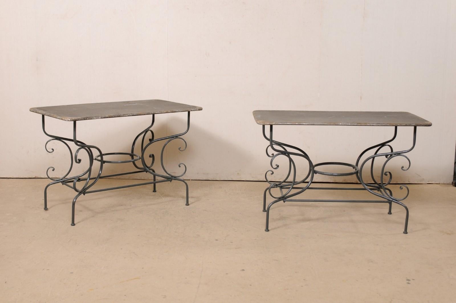 A French pair of metal occasional tables from the mid 20th century. This vintage pair of tables from France each feature textured, rectangular-shaped tops with rounded corners, which are raised upon four curvy metal legs, with large c-scroll