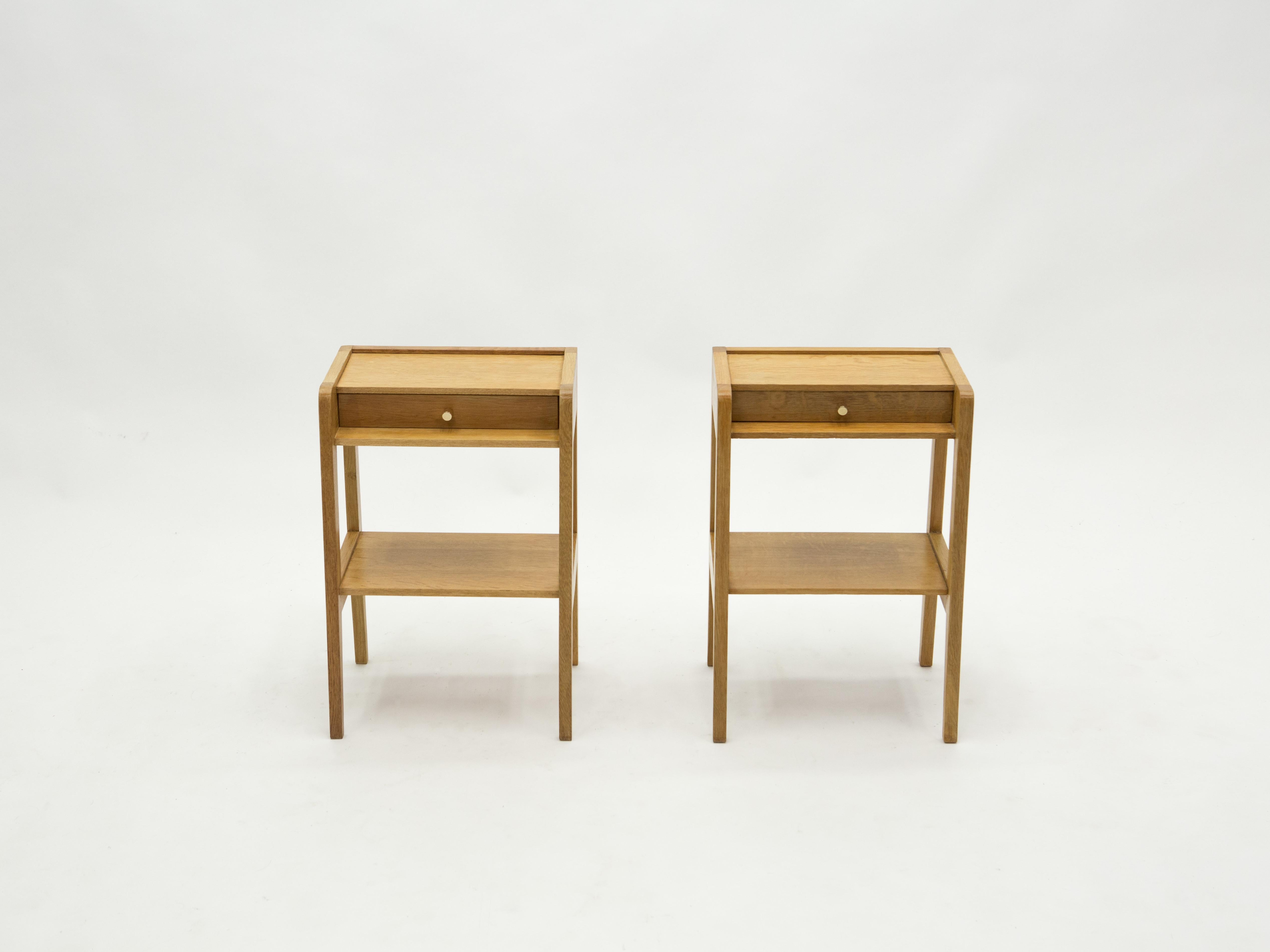 This pair of small lined and elegant modernist nightstands is made from oakwood in France in the early 1950s. Vintage and typically French post Art Déco modernism, they feature nice small brass handles and a nice two-tiered design. They have been