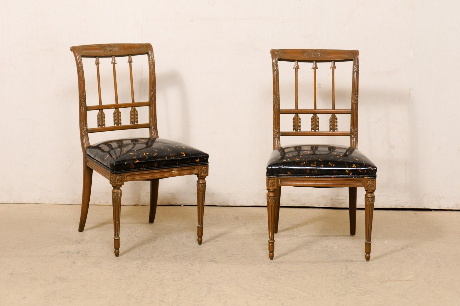A French pair of Neoclassical carved and painted wood accent chairs, with upholstered seats, from the mid 20th century. These vintage chairs from France feature beautiful arrow carved back-splats, set within a frame carved with urn and twined-reed