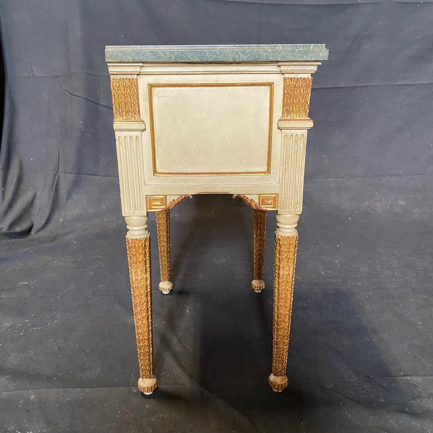 A French pair of neoclassical painted wood nightstands, bedside tables or side chests with original gold gilt and grayish ivory paint.  Each has lovely original marble tops, which rest above stunningly carved gold gilt friezes, all over hand
