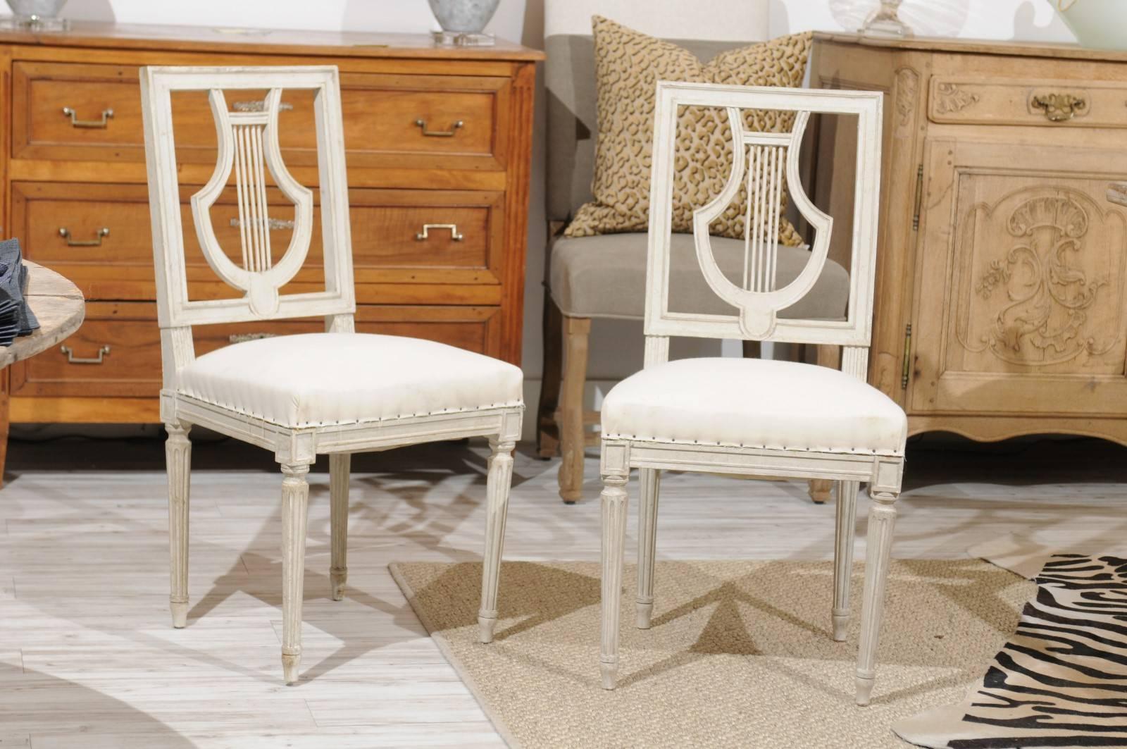 A pair of French painted wood dining room side chairs with lyre-shaped backs and fluted legs from the early 20th century. The chairs are priced and sold per pair, and we currently have one set. We're always on the hunt for exquisite dining chairs