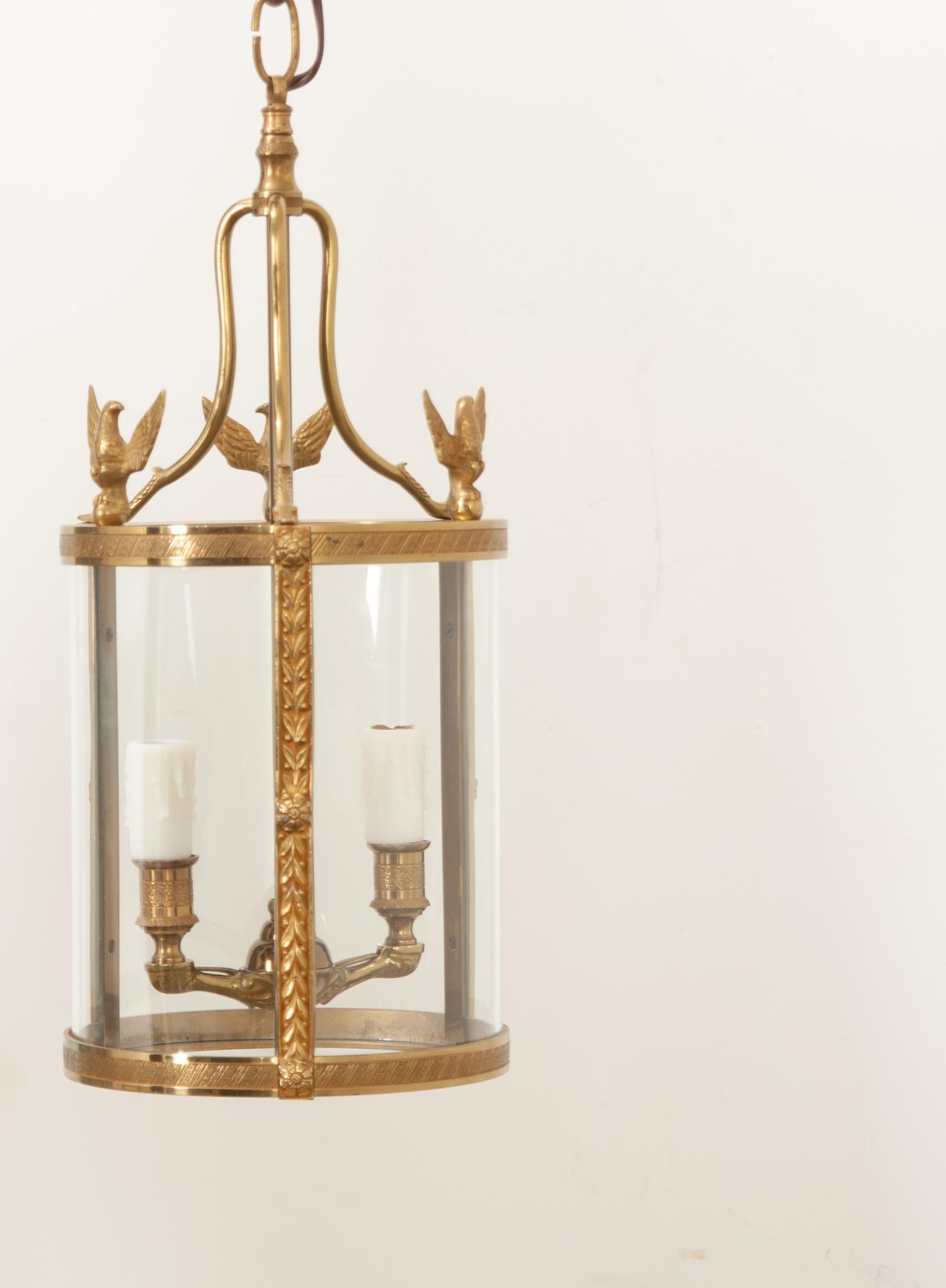 A petite French pair of brass lanterns with curved glass panels. This unique design has eagles at the top of the lanterns with decorative floral trim. Each lantern has two candle arms. Recently cleaned and rewired for the US using UL-listed parts,