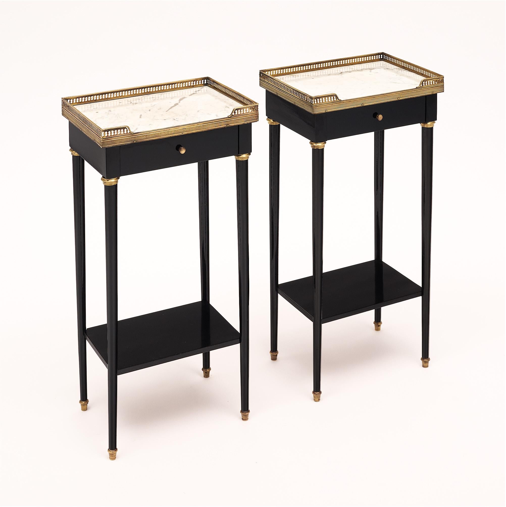 Pair of French side tables in the Louis XVI style. Original Carrara marble tops are surrounded with an opened brass gallery. Each table feature a dovetailed drawer and a bottom shelf. This pair is in very nice vintage condition with only minor