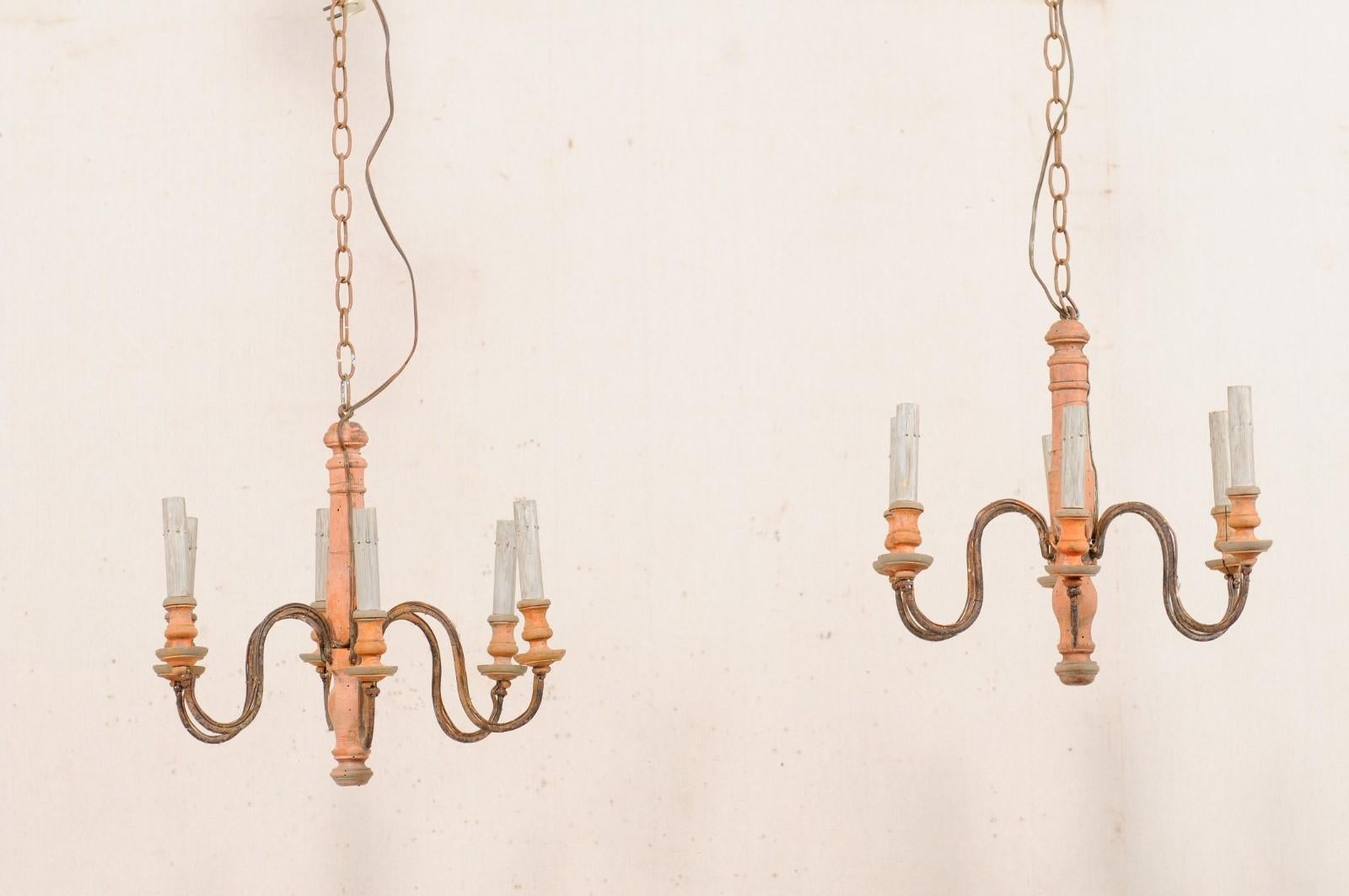 A French pair of painted wood column six-light chandeliers from the mid 20th century. This vintage pair of chandeliers from France each features a carved/turned central wooden column from which six s-scrolled iron arms emerge outward from the