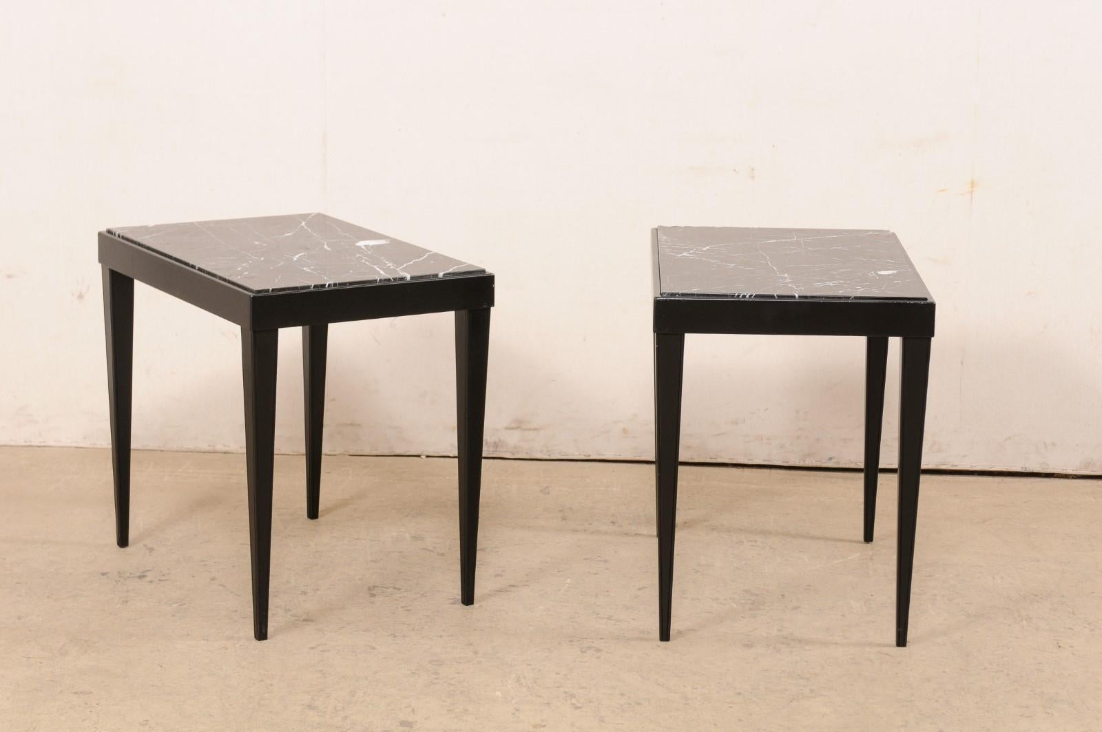 A French pair of black painted wood side tables with marble tops from the mid 20th century. These vintage end tables from France have been designed in clean/modern lines. Each featuring a rectangular-shaped marble top, within a linear frame with