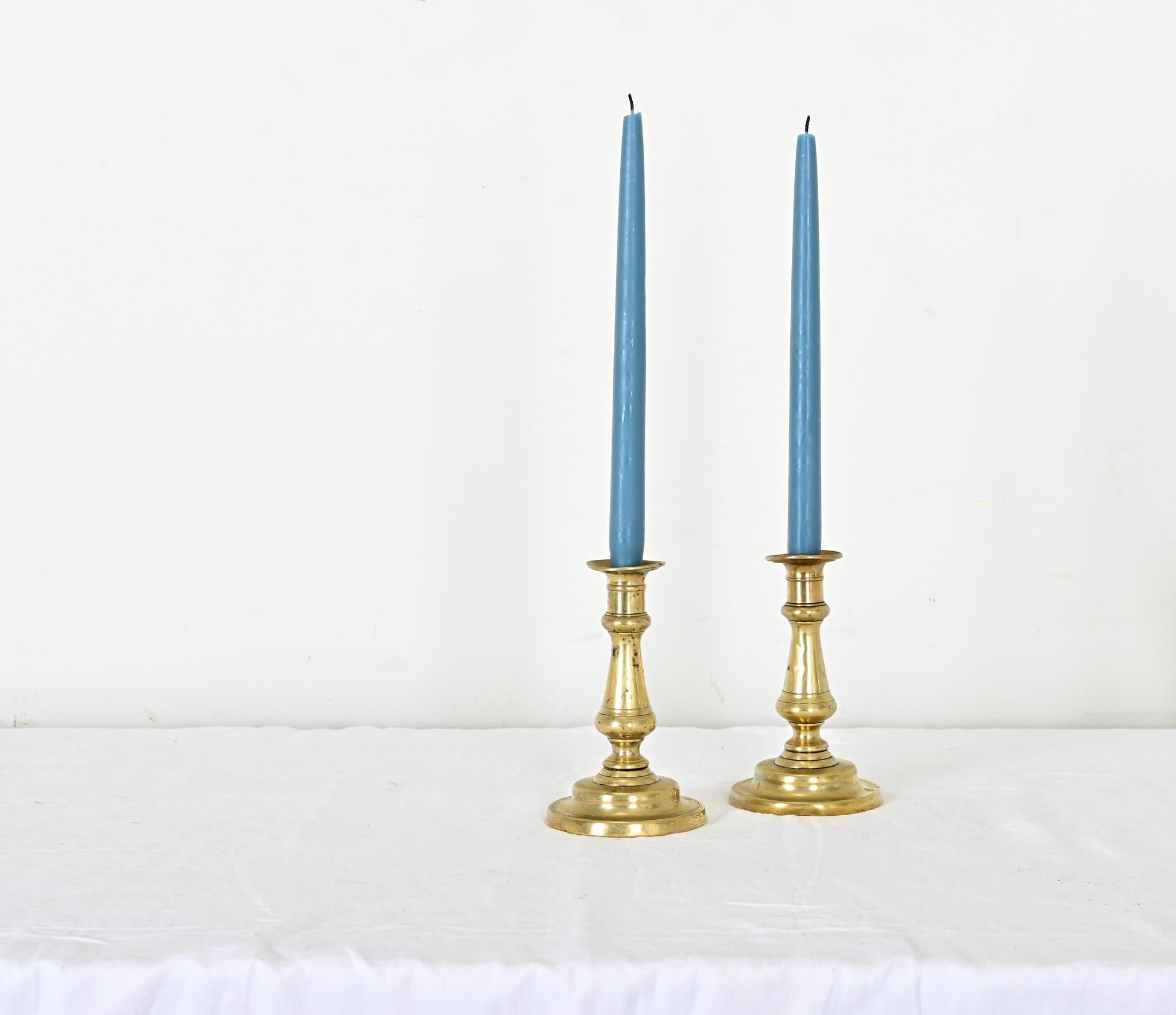 Una piccola coppia di candelieri francesi del XIX secolo, in ottone massiccio e lucente. La pesante base è fusa con forme lisce e arrotondate e, nonostante una certa patina, il metallo risplende brillantemente. Con un'altezza di poco superiore ai 15