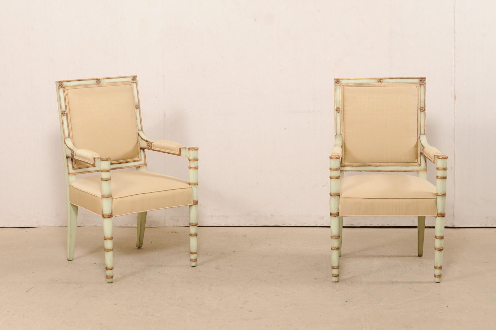 A pair of vintage French painted wood and upholstered armchairs. This pair of accent chairs from France each feature upholstered square-shaped and upholstered backs, nicely set within a frame adorn with sweetly carved flower heads. The chairs are