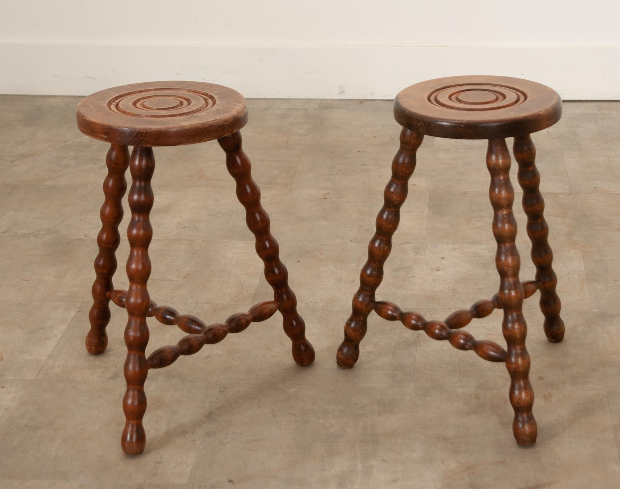 Direct from France, a pair of superb hand-carved vintage French stools. This distinctive pair of stools has attractive, relief carved tops featuring a double circular design pattern. Splayed “bobbin” turned legs and cross stretchers, gorgeous wood