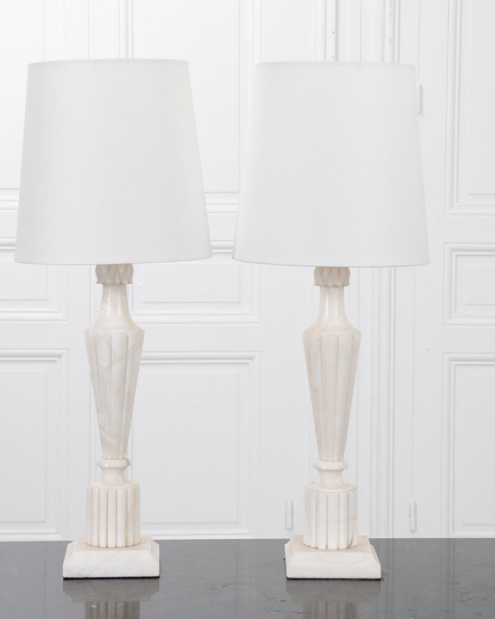 An elegant pair of vintage lamps from France! Carved from beautiful white marble with reeded details. The lamps come with fine custom white linen shades, measuring 10” diameter. Sleek and monochromatic, this pair of lamps will brighten up any space