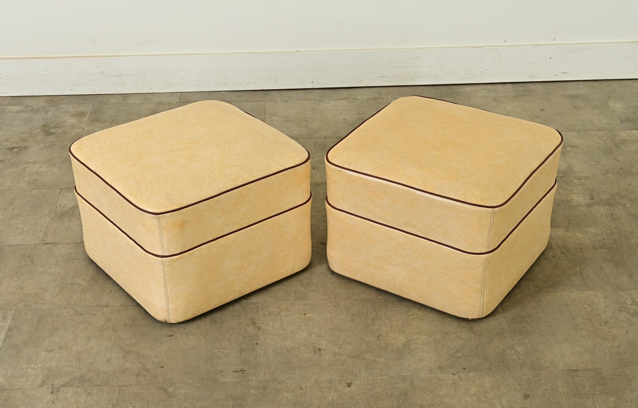 Versátil par de taburetes-escabel franceses, vintage años 70, tapizados en piel sintética beige para mayor durabilidad y acentuados con ribetes marrones. Cómodos tanto para sentarse como para descansar los pies, estos reposapiés cuadrados están en