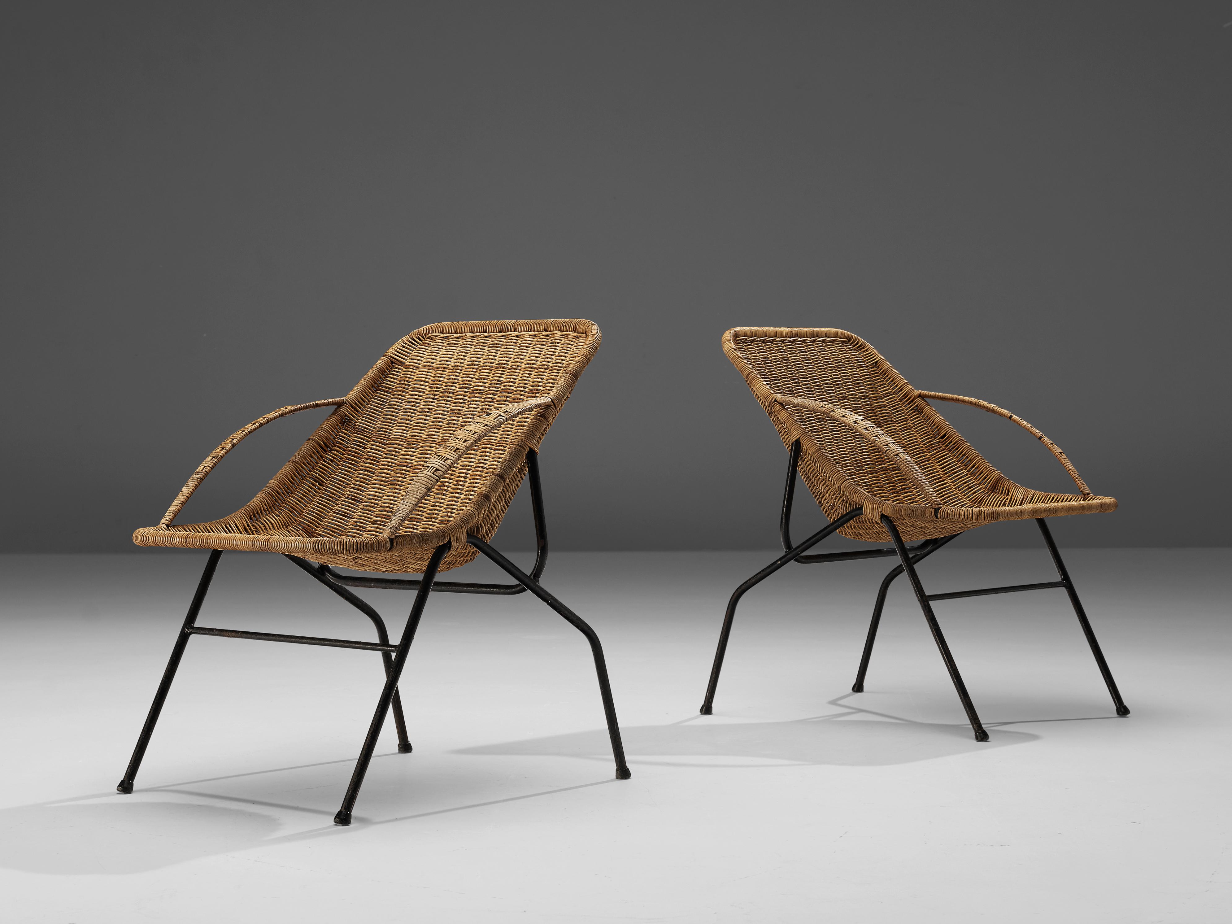 Armchairs, rattan, cane and black coated metal, France, 1950s. 

This pair of cane chairs are executed with a rattan shell with two woven cane armrests. The seat are slightly tilted. The frame is black and sculptural and the chairs show strong