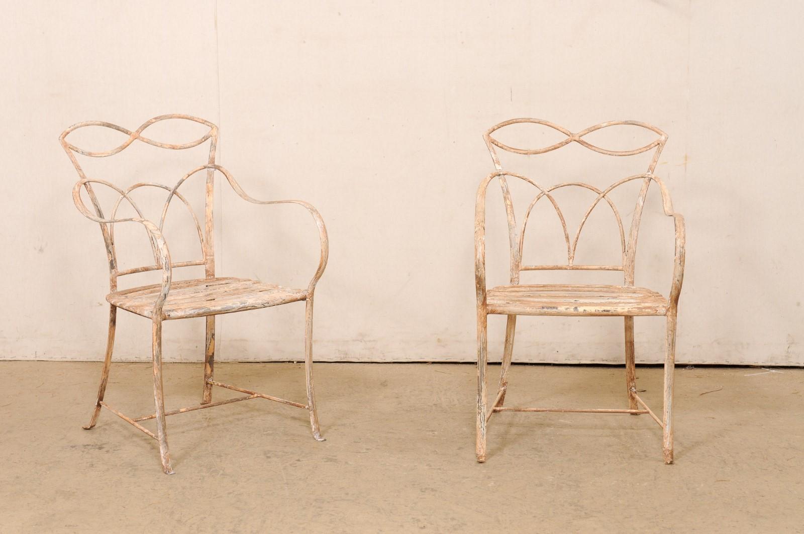 A French pair of painted iron patio conversation chairs. This vintage pair of iron chairs from France have nicely designed backs that are open with an intertwining lattice design with almond and arch shapes, that give these chairs a light and airy