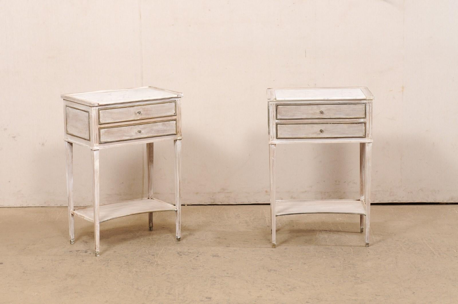 A French pair of painted wood side chests, with marble tops and brass accents, from the mid 20th century. These mid-century commodes from France each feature a rectangular-shaped with fixed/recessed white marble, surrounded with a raised lip on