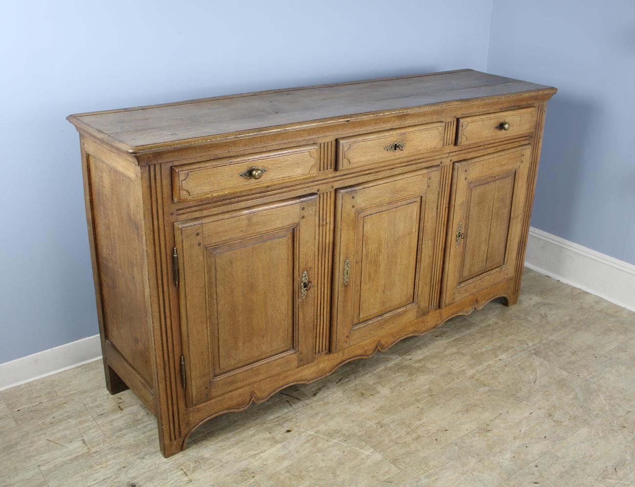 A handsome enfilade or three door French oak buffet with mellow oak grain, color and patina. The carved panels on the doors and sides give this simple sturdy piece a note of good design interest.
