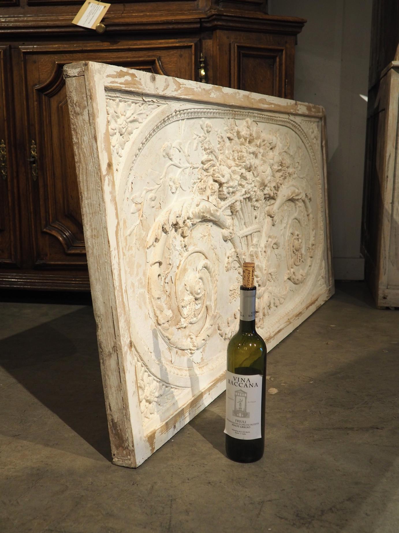 This beautiful parcel painted plaster and wood panel from Provence, France was made in the Louis XVI style.  It features a bas-relief rendering of a pair of foliate rinceaux emanating from a vase overflowing with a bouquet. The plaster is