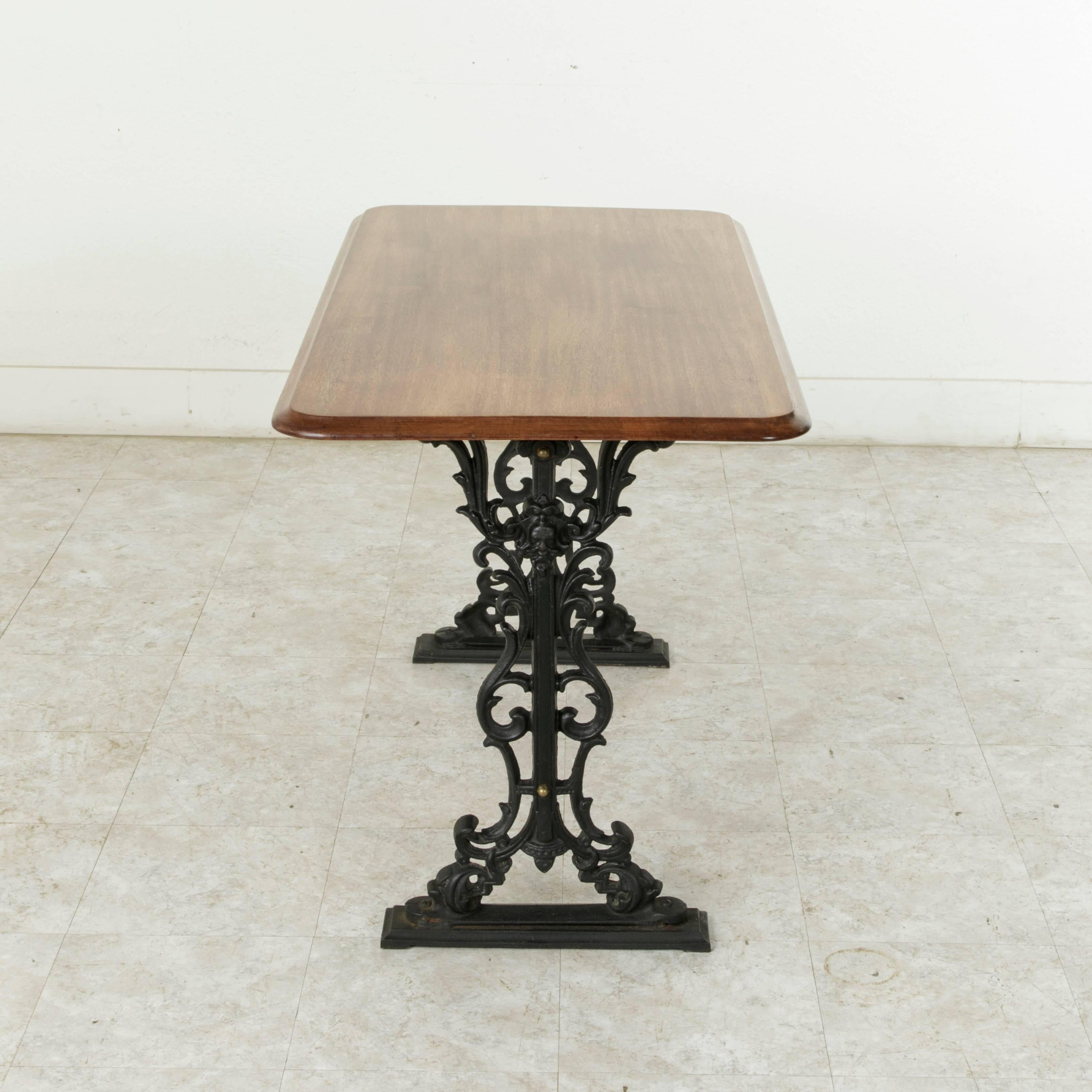 This turn of the 20th century French Paris bistro table features a cast iron base of intricate scrolling and its original solid mahogany top. The base measures 40 inches in length and 16 inches in width and has a vertical X-stretcher that provides