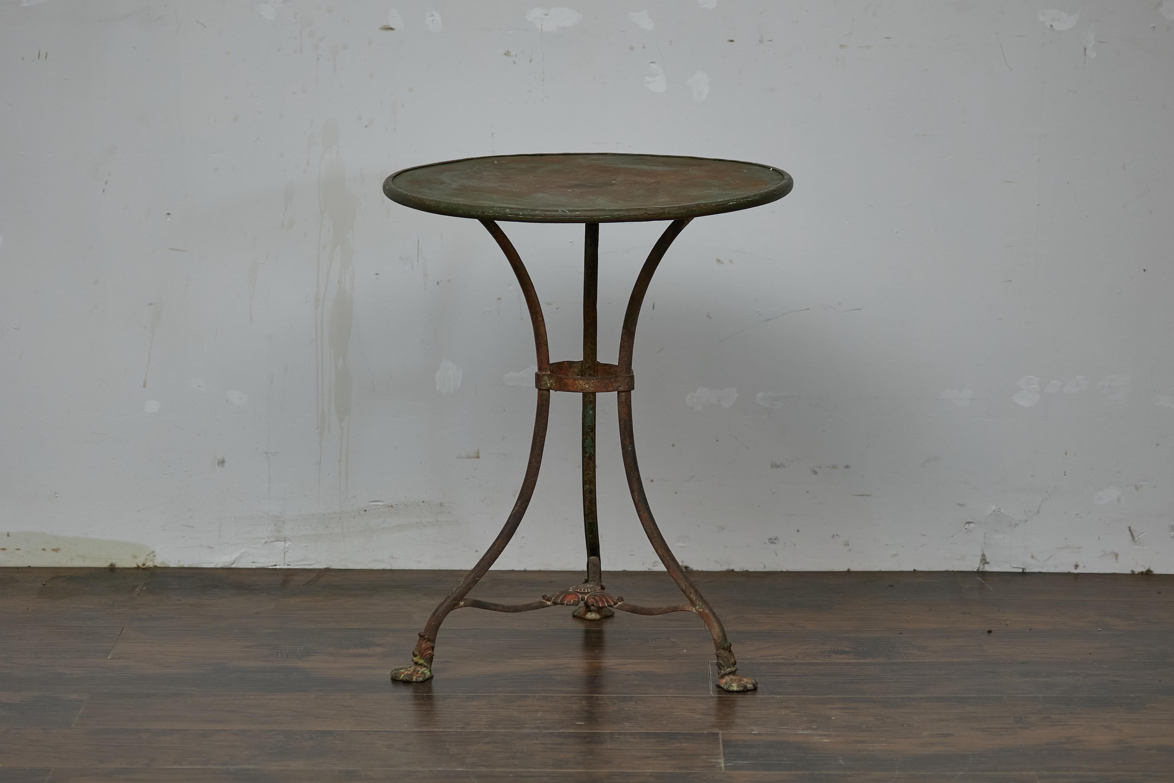 Rustic French Parisian iron garden or patio table from circa 1900 with circular top, tripod base and rusty patina. This rustic French Parisian iron garden or patio table from circa 1900 captures the timeless charm of a Parisian courtyard with its