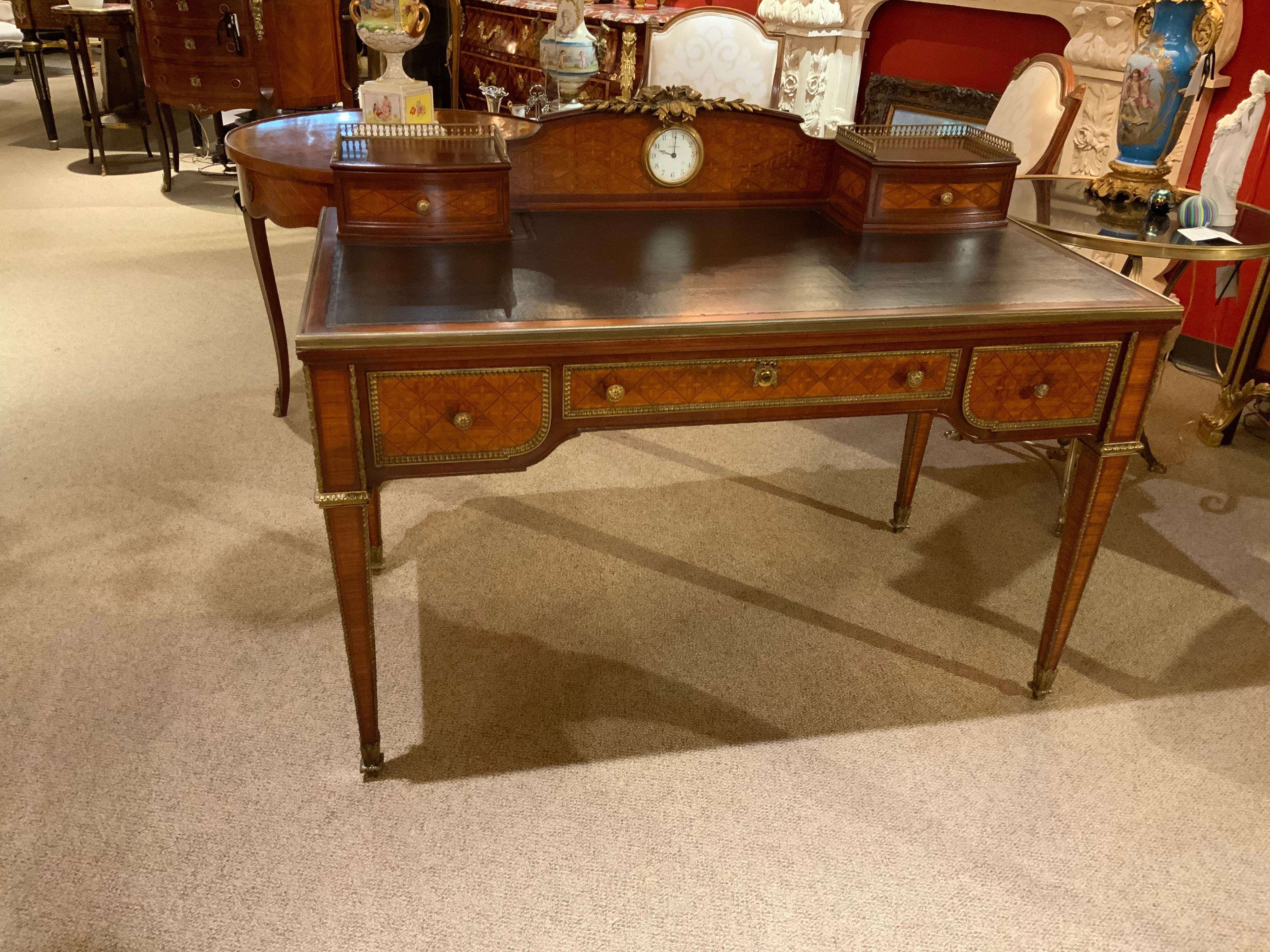 Nicely inlaid parquetry and marquetry with ornate bronze mounts. Black leather top
Three drawers across the front and two petite cabinets on the surface with drawers.
A clock is mounted at the center marked Seth Thomas.
Signed Paris on the center