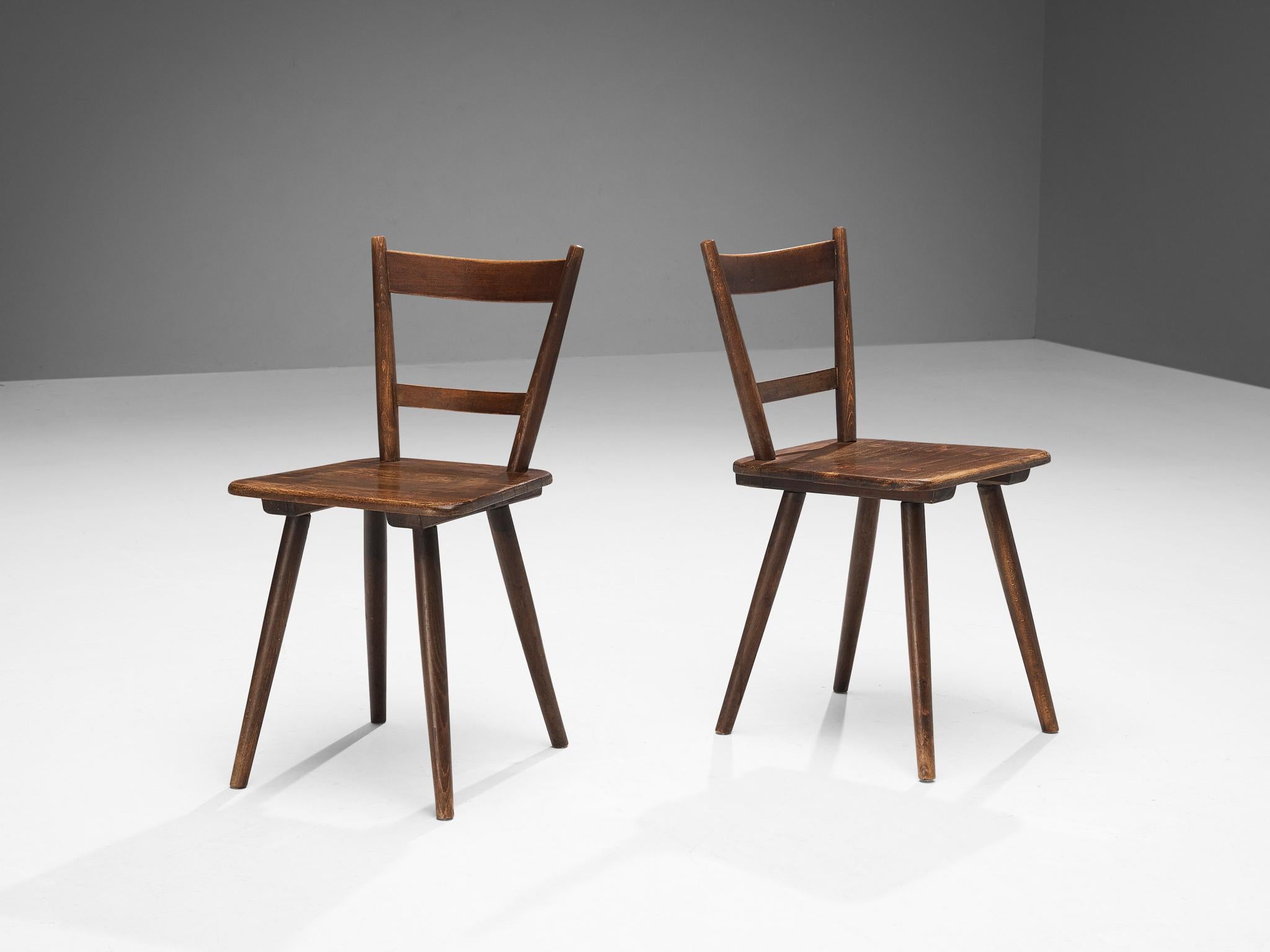 Pair of dining chairs, stained wood, France, late 1940s. 

Rustic pair of dining chairs manufactured in France. Simple yet stylish, these chairs feature a modest frame with sleek, elegant elements. Note for example the tapered legs slightly