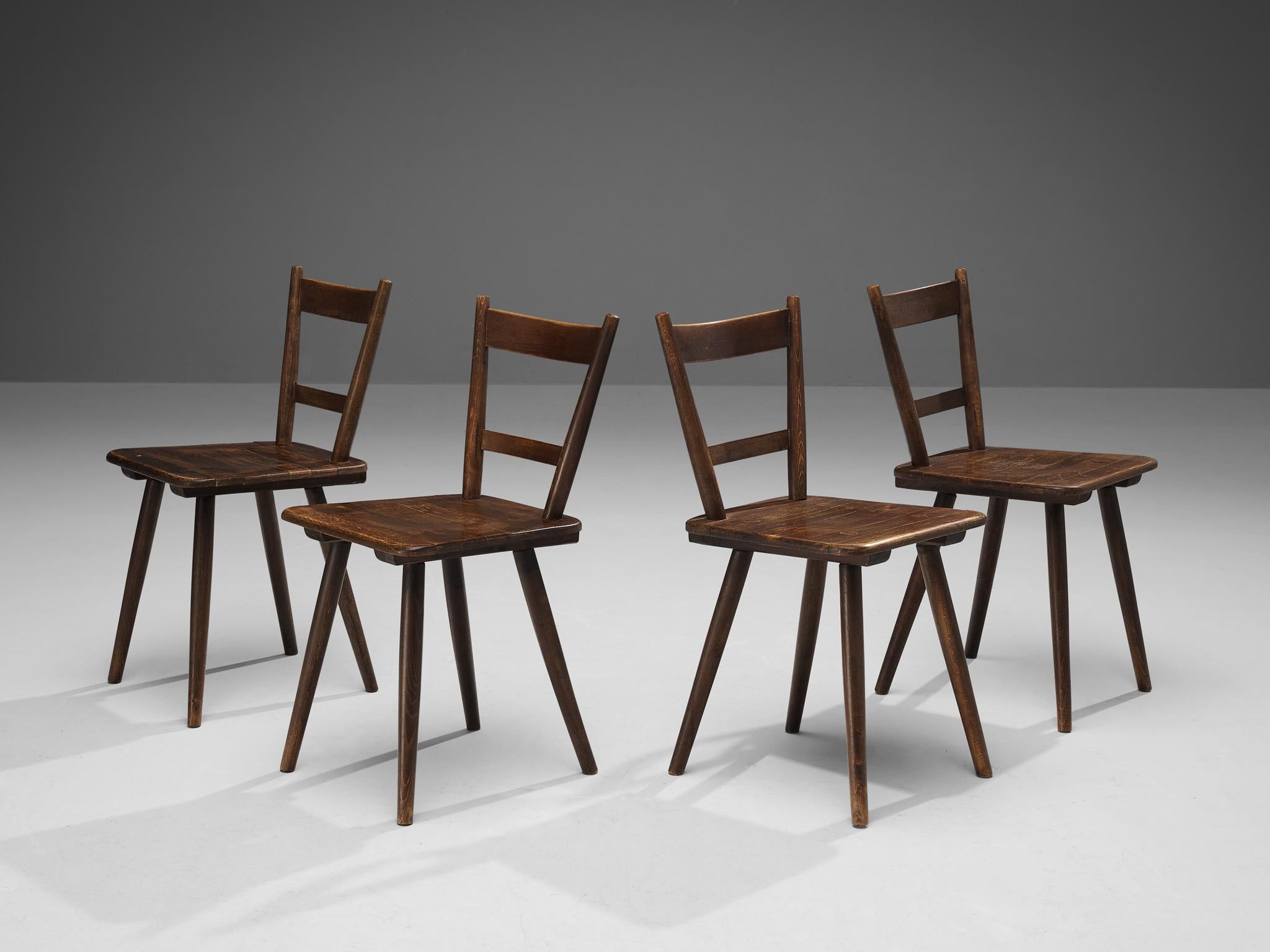 Set of four dining chairs, stained wood, France, late 1940s. 

Set of four rustic dining chairs manufactured in France. Simple yet stylish, this chair features a modest frame with sleek, elegant elements. Note for example the tapered legs slightly