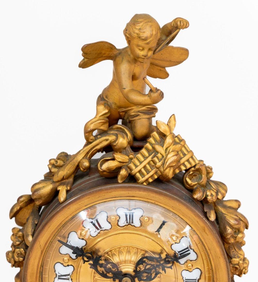 Pendule de cheminée française en bronze patiné et marbre, fin du 19e siècle, cadran circulaire, avec mouvement d'horlogerie,  surmonté d'un angelot jouant du triangle, sur un piédestal effilé et une base rectangulaire en marbre moucheté centrée par
