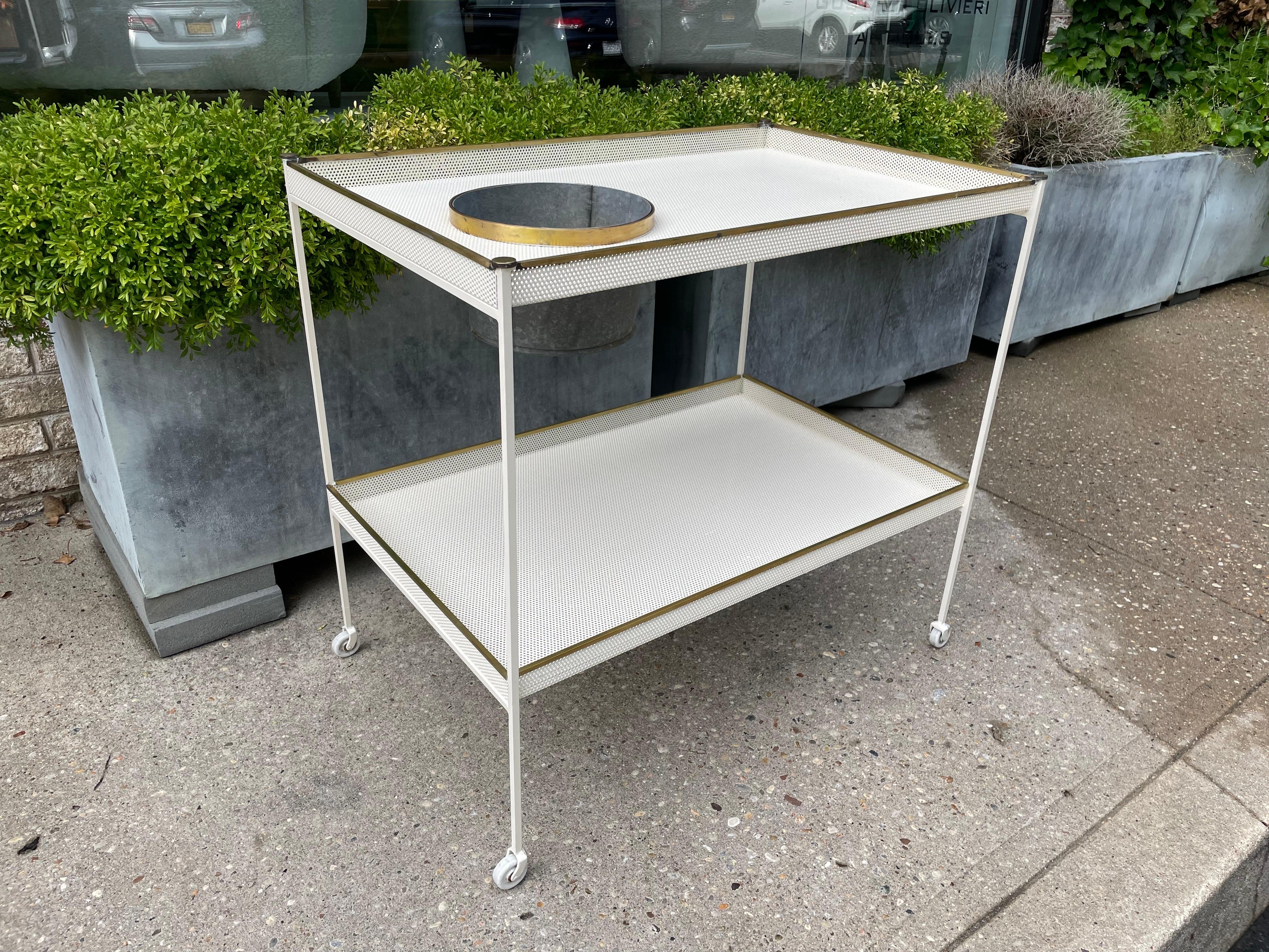 This is a wonderful two-tiered perforated metal in off-white with Porcelain wheels.  Brass accents throughout and a removeable galvanized metal ice bucket for chilling wine or champagne.  Great amount of surface space for entertaining.  Mategot