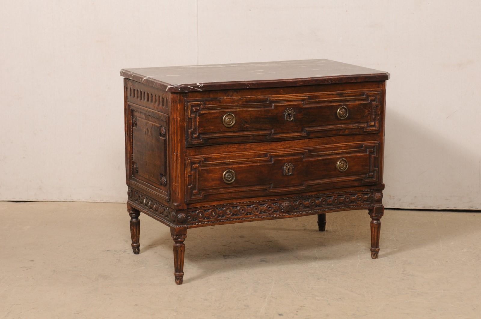 A French Neoclassic carved-wood chest of drawers with marble top from the early 19th century. This antique commode from France features a merlot marble top, resting upon a beautifully carved case, with subtle serpentine-shape, that houses a pair of