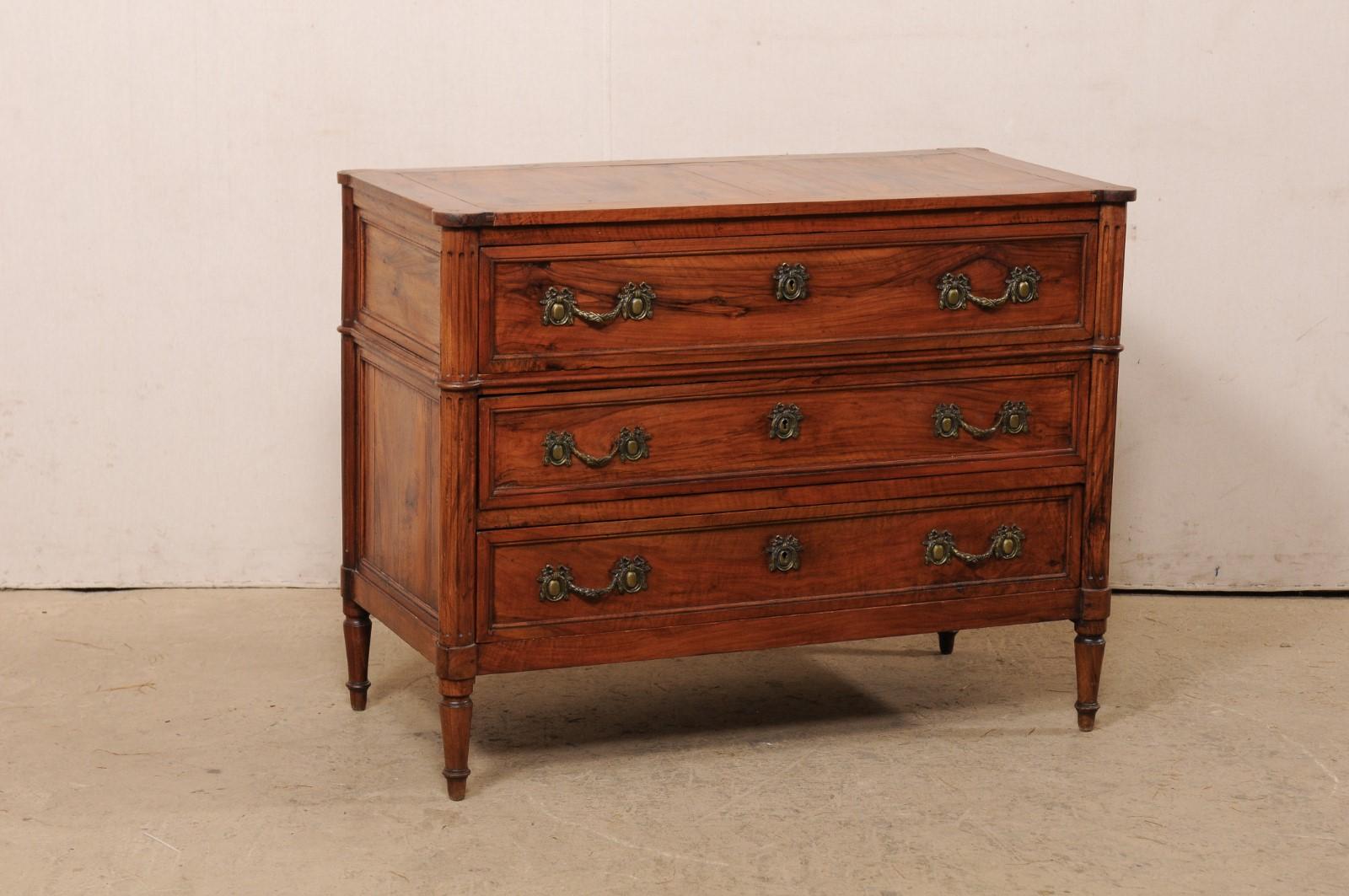 A French neoclassic carved-wood commode from the 19th century. This antique chest from France features a top with rounded/cove-edges at four corners, atop a neoclassical case with rounded and flute-carved side posts, three full sized drawers, and