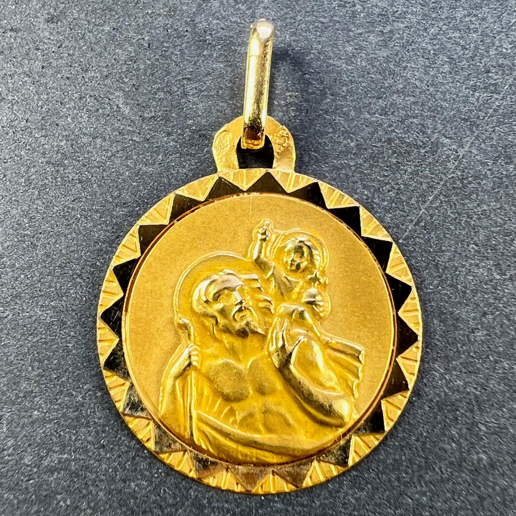 A French 18 karat (18K) yellow gold charm pendant designed as a medal depicting St Christopher as he carries the infant Christ across a river within a sunburst frame of polished and textured gold. Stamped with the eagle’s head for French manufacture