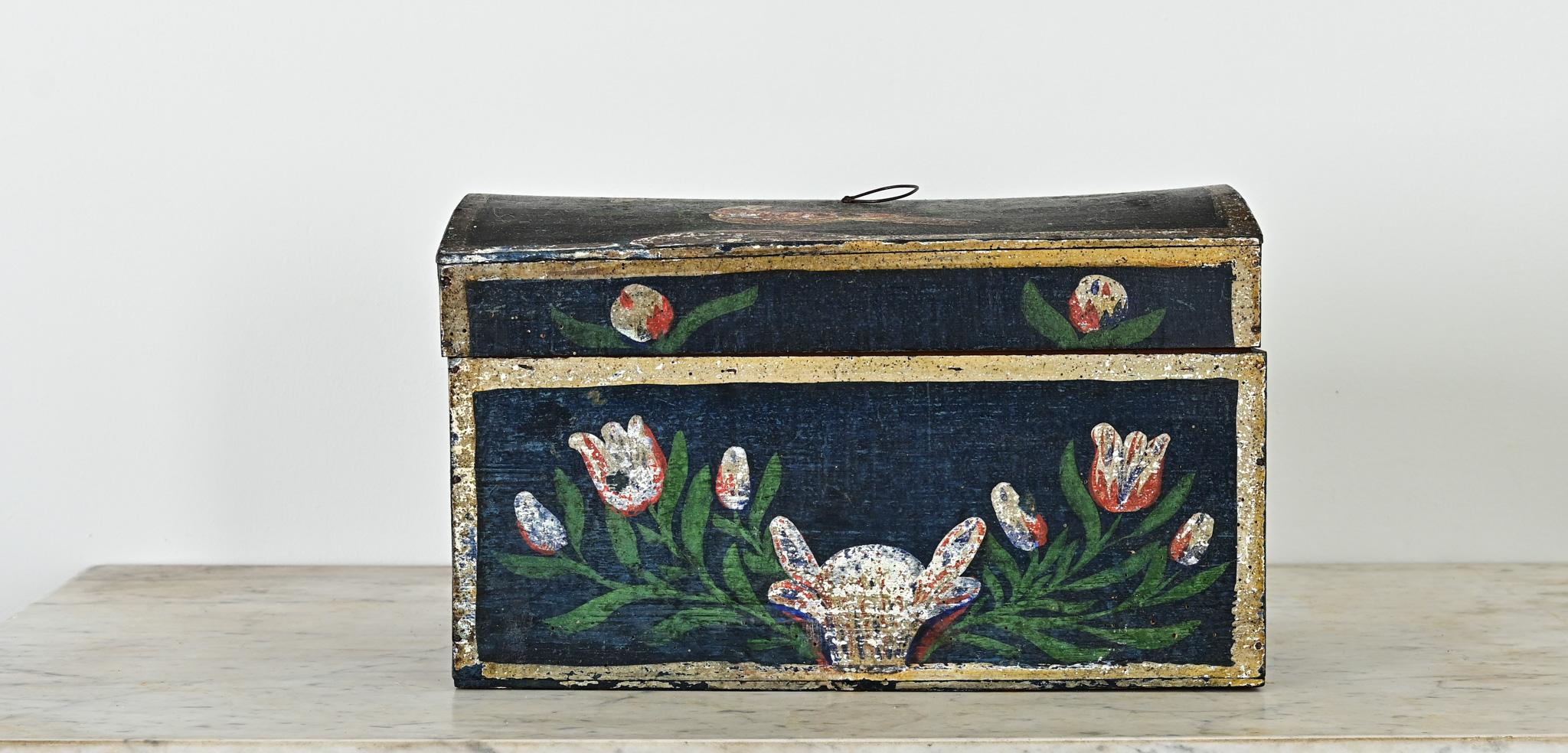 A fantastic antique marriage or bridal box–from Normandy, France–decorated with hand-painted floral details that grace every surface, including a small bird on the top. Vibrant pink and cream painted tulips on a dark blue background have aged
