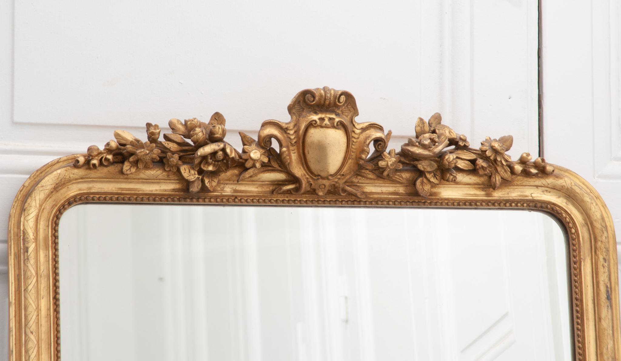 The perfect petite Louis Philippe style mirror for your mantel or small space! The giltwood frame has a continuous zig zag pattern on the outer frame and bead pattern closer to the mirror plate. A large crest of highly carved flowers and shield