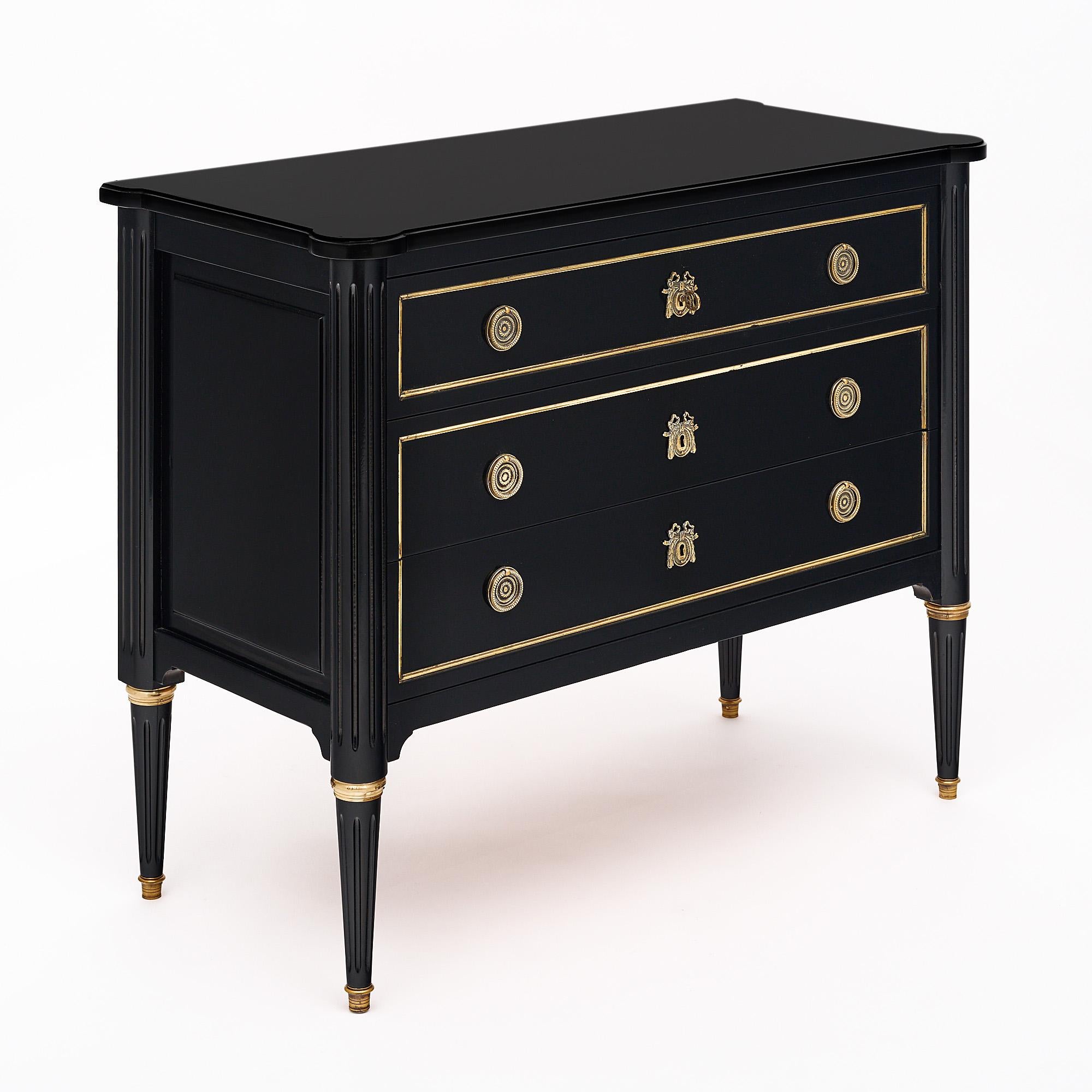 Chest of drawers, French, Louis XVI style, of mahogany, three dovetailed drawers, four tapered and fluted legs, the petite commode is  ebonized and finished in a lustrous Museum quality French polish, gilt brass throughout and finely cast hardware.