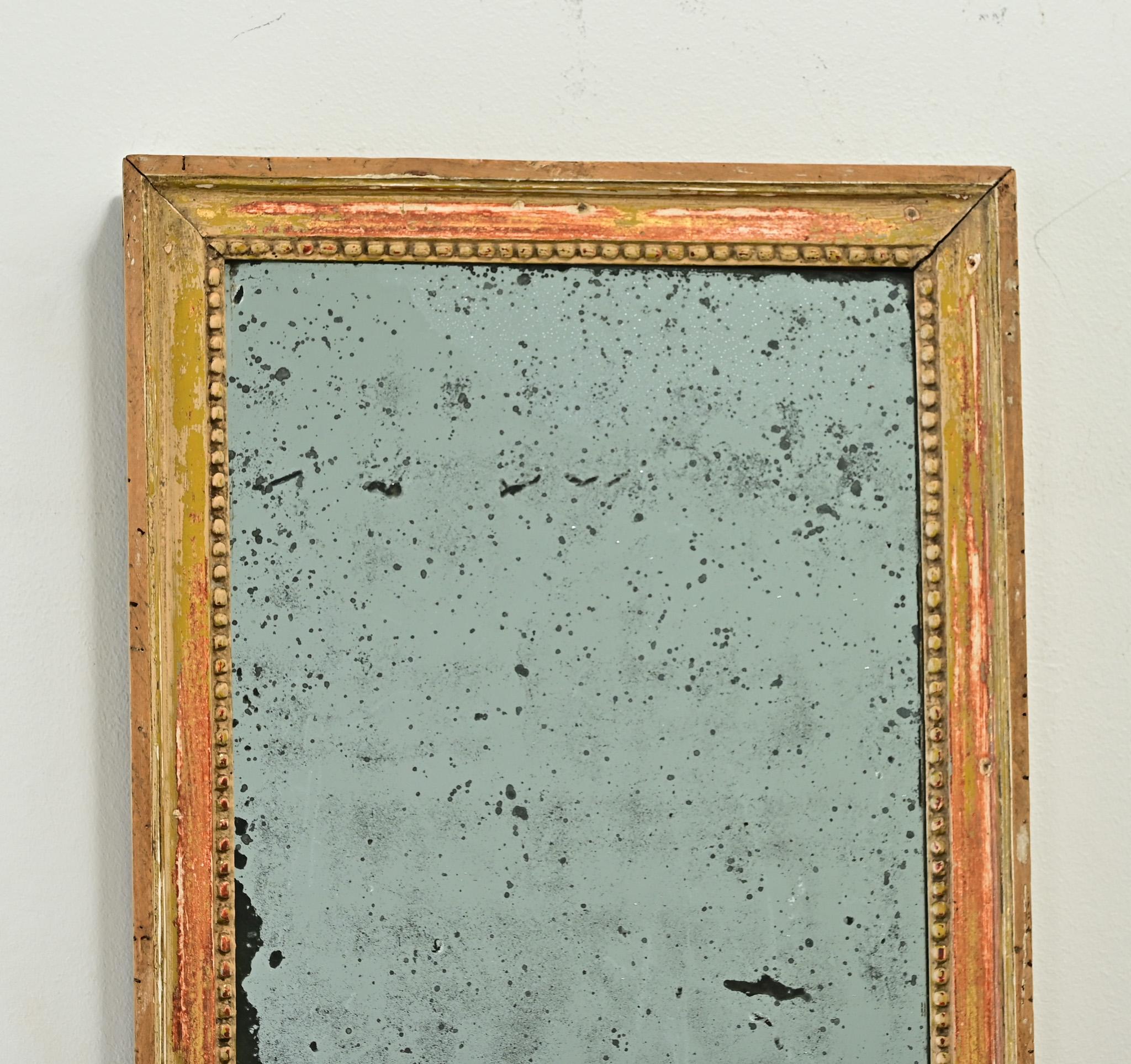 A petite French gold gilt mirror made in the Louis XVI period. This hand carved frame has its original painted and gold gilt finish revealing the reddish bole beneath. The symmetrical frame has interior beading and holds its original mirror plate