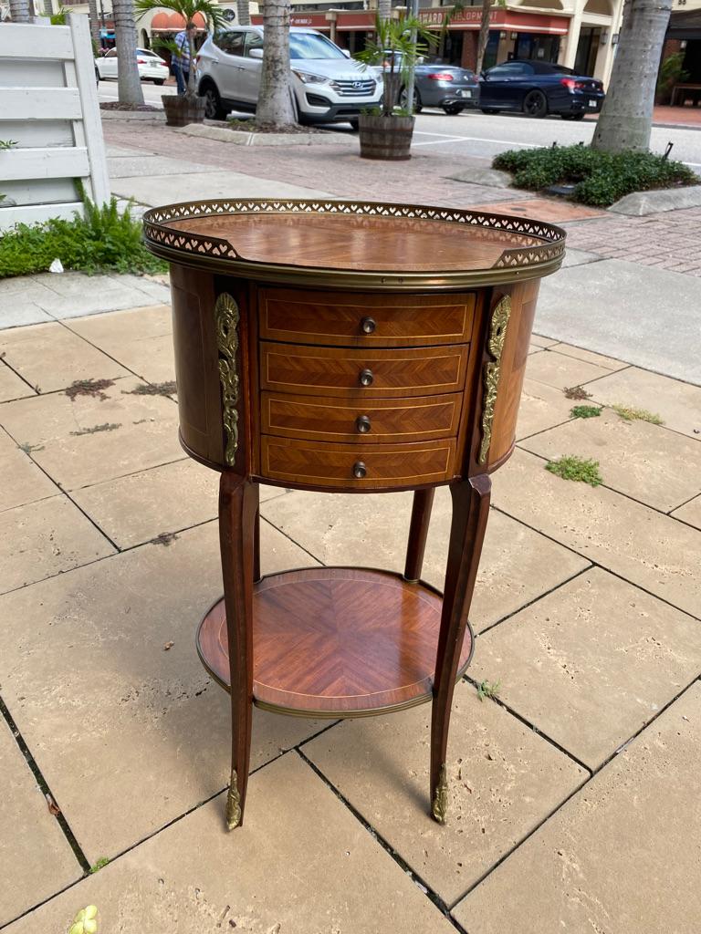 French petite oval shaped side table marquetry design with partial gallery surround. 4 mini drawers top and center, ormolu embellishments, small round shelf on the bottom.