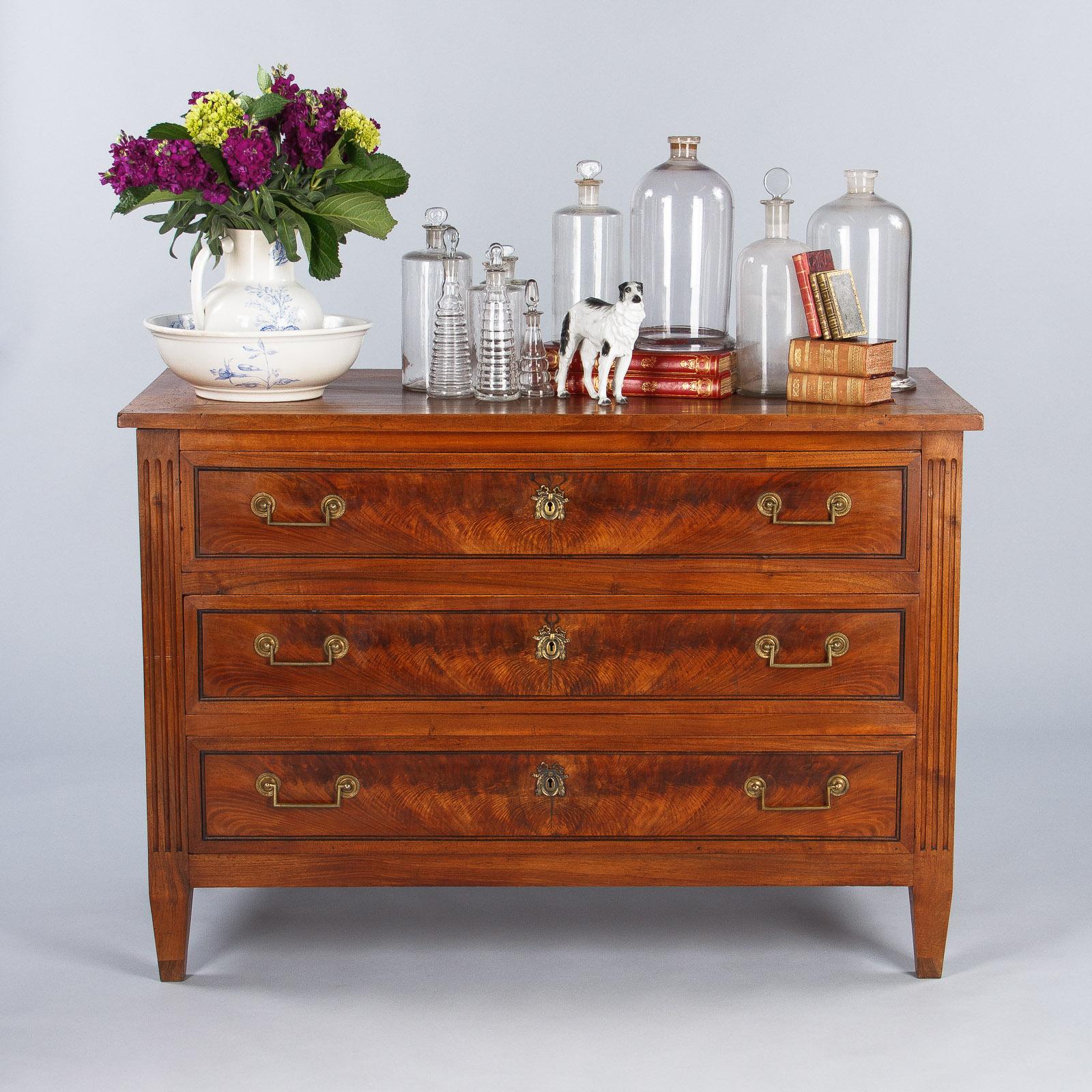 A clear glass tall pharmacy jar, French circa early 1900s. Clear glass blown into a mold with straight sides and a slight curve at the shoulders. A short neck leads to a flared rim mouth that holds a fitted glass stopper with a flat, rounded handle.