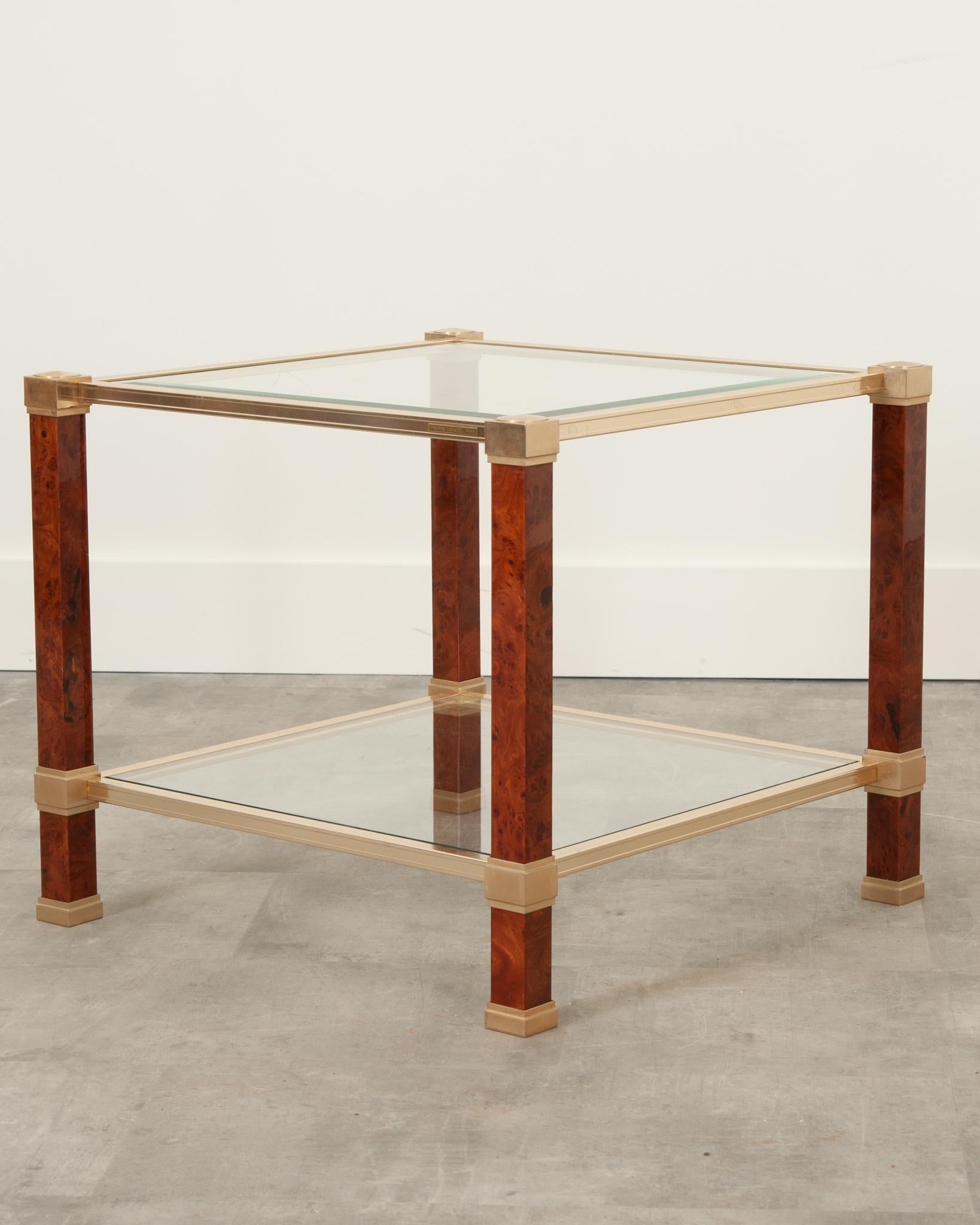 A square vintage French cocktail or coffee table with a unique flair. The frame is made of brass and supported by square acrylic legs. Snuggly enclosed in brass, the top glass is beveled with a small chip at one corner. The lower tier glass is in
