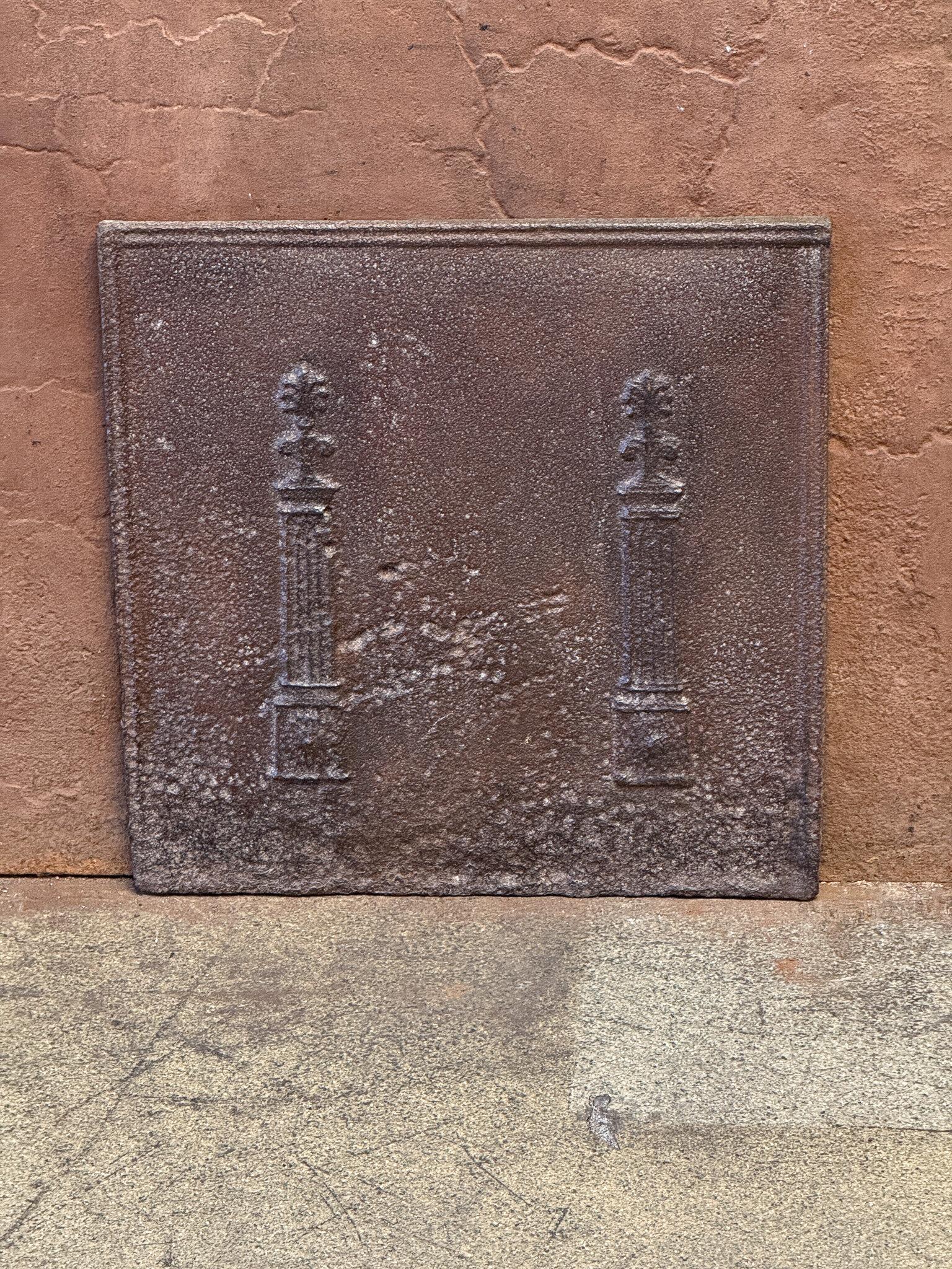 19th century neoclassical fireback with two pillars of freedom. The pillars symbolize the value liberty, one of the three values of the French revolution. 

The fireback is made of cast iron and has a natural brown patina. Upon request it can be