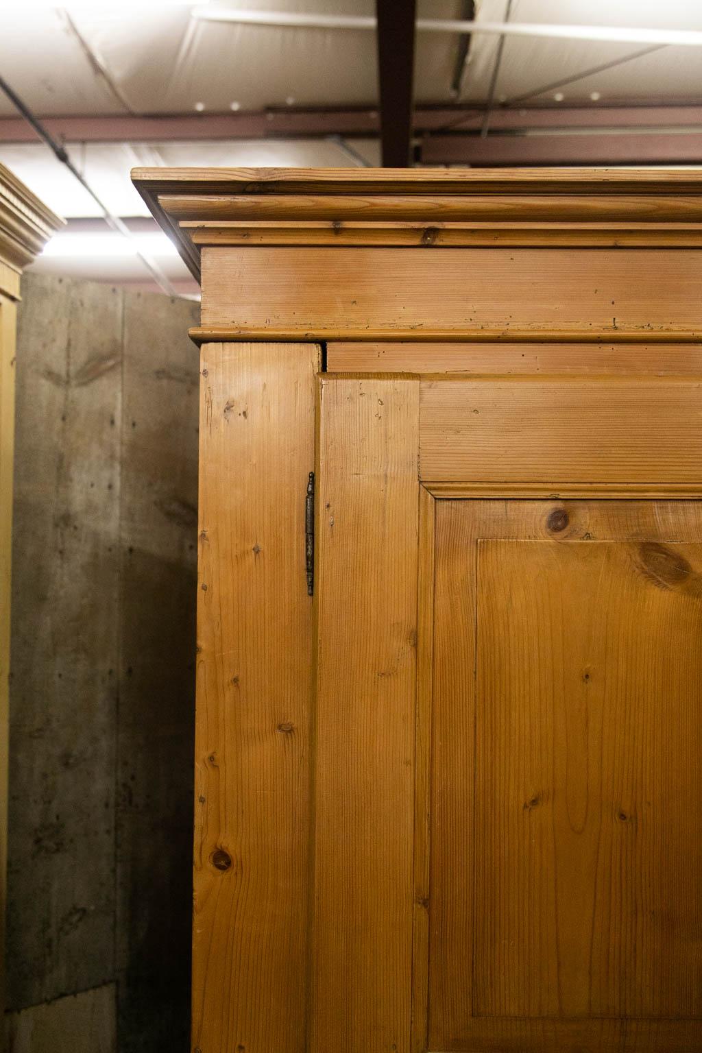 The interior of this armoire is open. The doors have two raised panels framed with carved moldings. The sides have one long panel framed with carved molding. There are two working drawers below the doors in the base which terminates in bun feet.