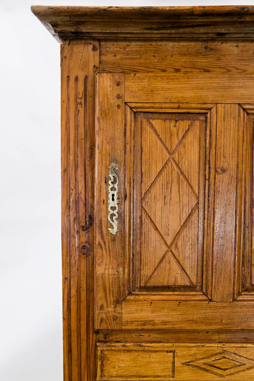 The upper and lower doors of this bonnetiere have exposed double peg construction with raised panels having diamond marquee carvings framed by shaped moldings. The stiles are triple fluted from top to bottom. The brass barrel hinges are original.