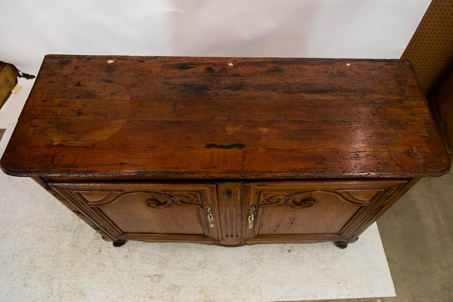 The sides of this buffet have recessed panels. The doors are framed with carved scrollwork. The center panel is fluted. There is exposed double peg construction. The corner stiles are rounded and terminate in scroll feet. The escutcheons are later.