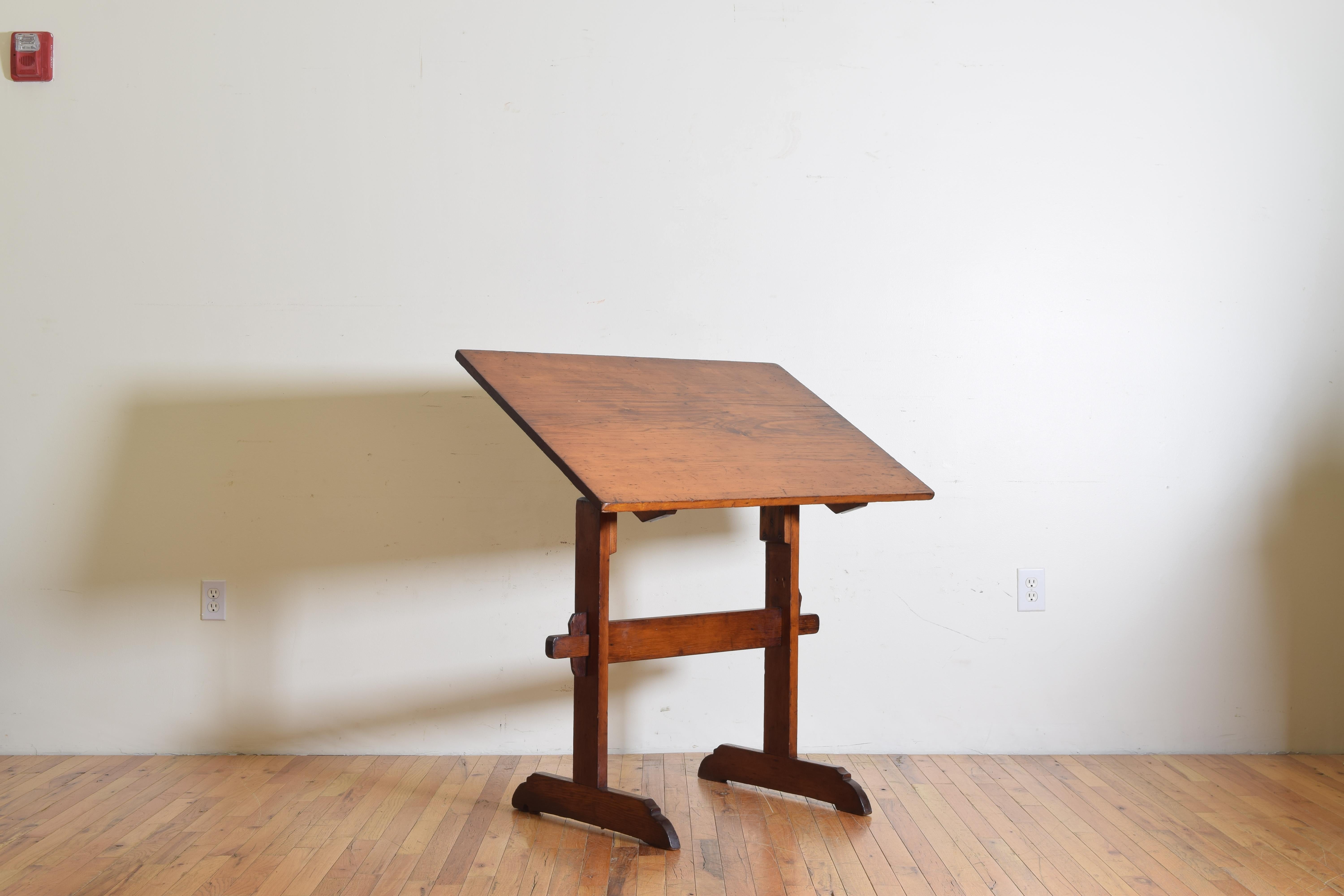 The adjustable rectangular top resting upon trestle-form legs and having iron notched dials for securing the top, joined by a vertical stretcher, raised on elongated bracket feet, height suitable for standing or setting on a stool.