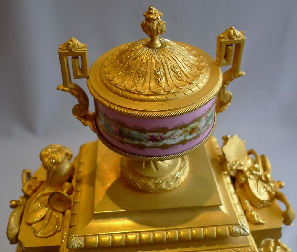 An attractive French Napoleon III antique mantel clock in original ormolu and fine pink, handpainted and jewelled porcelain. The clock sits upon its original giltwood base and has six feet to its D-ended base which is decorated with applied ormolu
