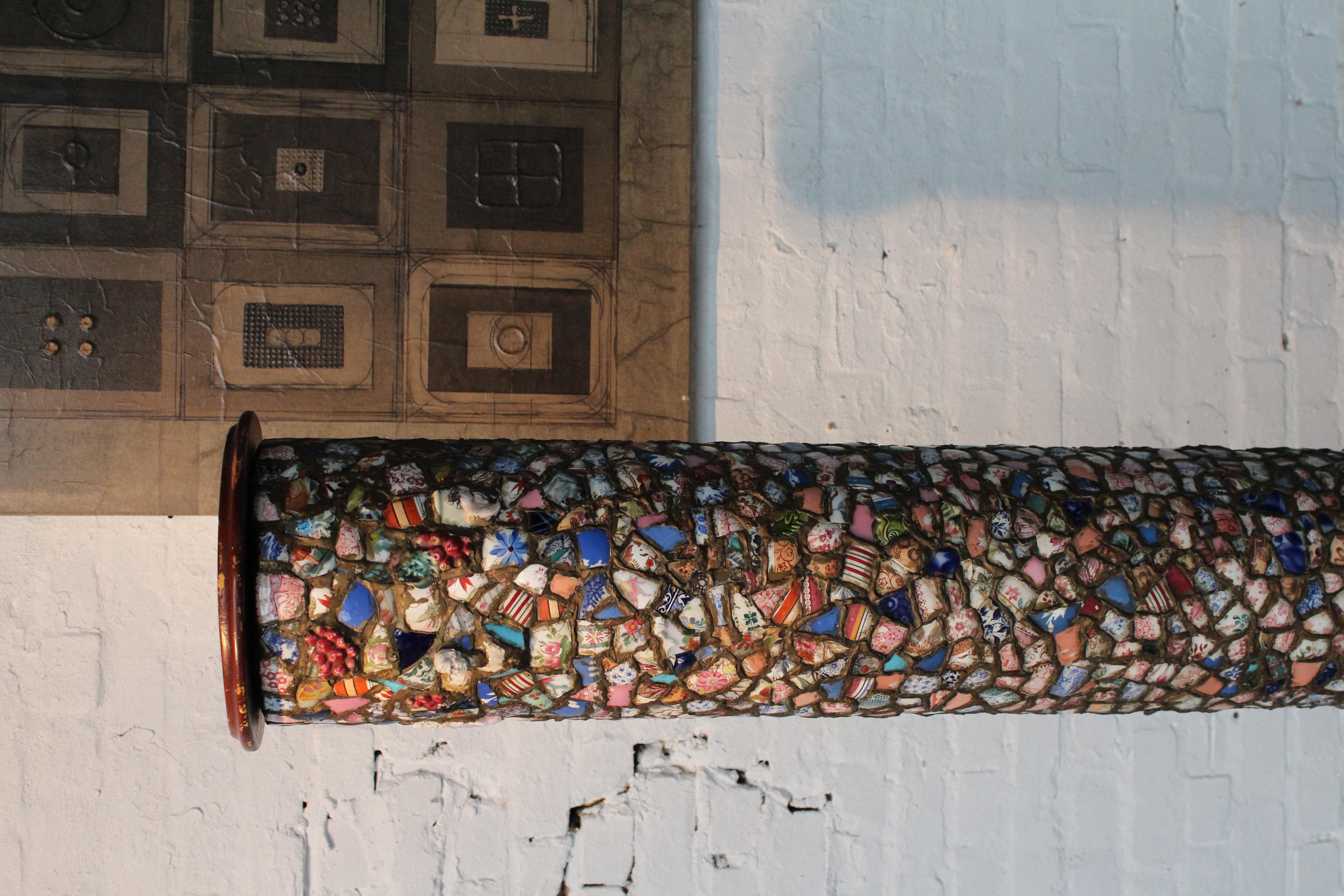 Grande colonna francese in piqué assiette con base in legno (diametro 50 cm) e rotelle in ottone. Il piano in legno ha un diametro di 27 cm. Il piqué assiette è uno stile di mosaico che incorpora frammenti di ceramica, piatti rotti e altri oggetti