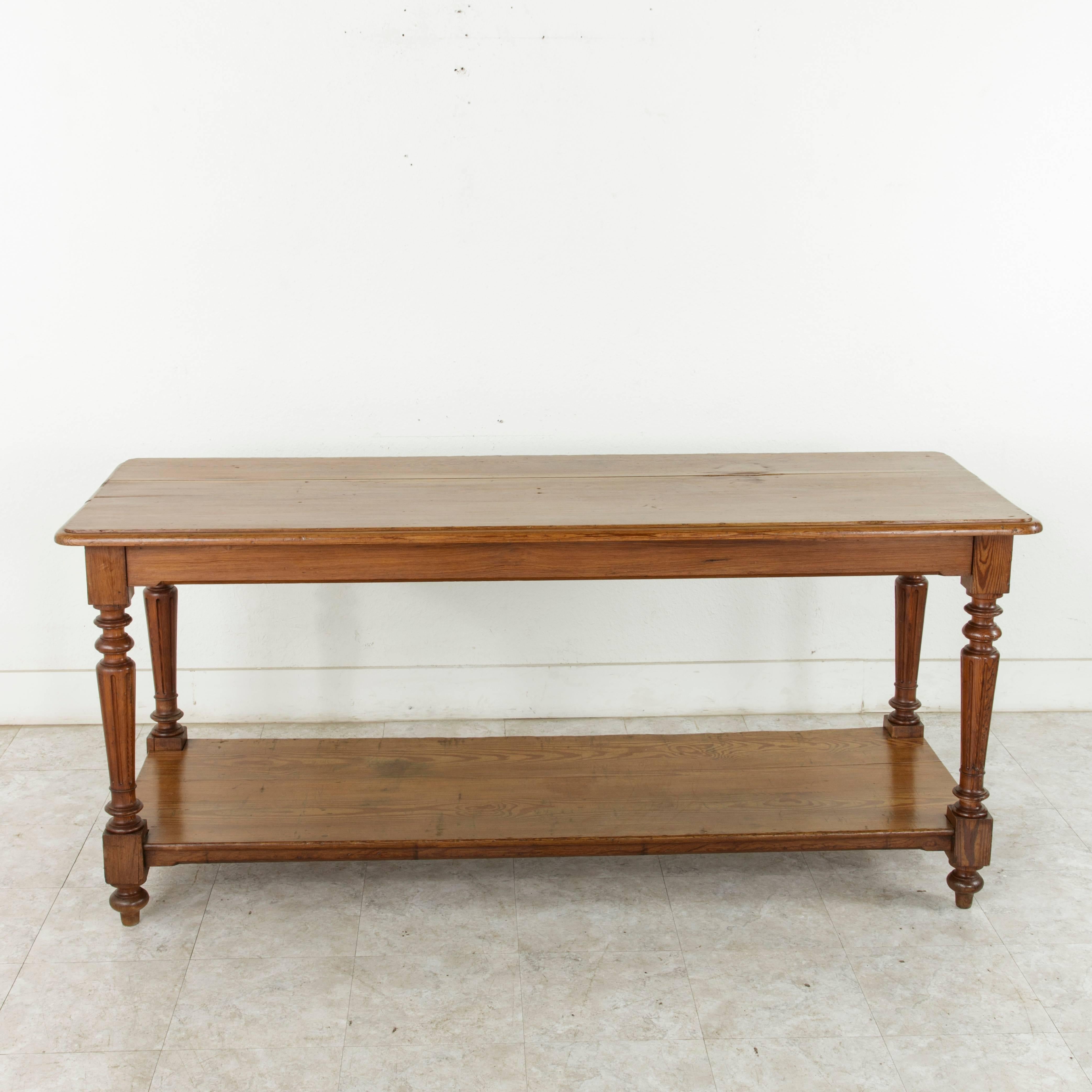 Originally used in a French fabric store to lay out and cut fabric around the turn of the twentieth century, this solid pitch pine fabric presentation table rests on tapered turned and fluted legs which support its lower shelf. The beveled top is